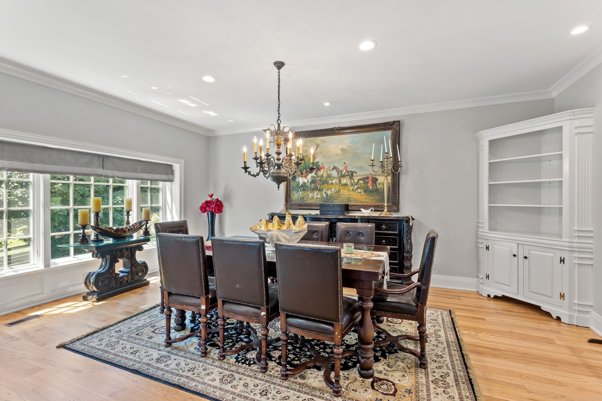 Formal dining room with chandelier, dark wood table, and chairs, with a large painting and built-in cabinet.