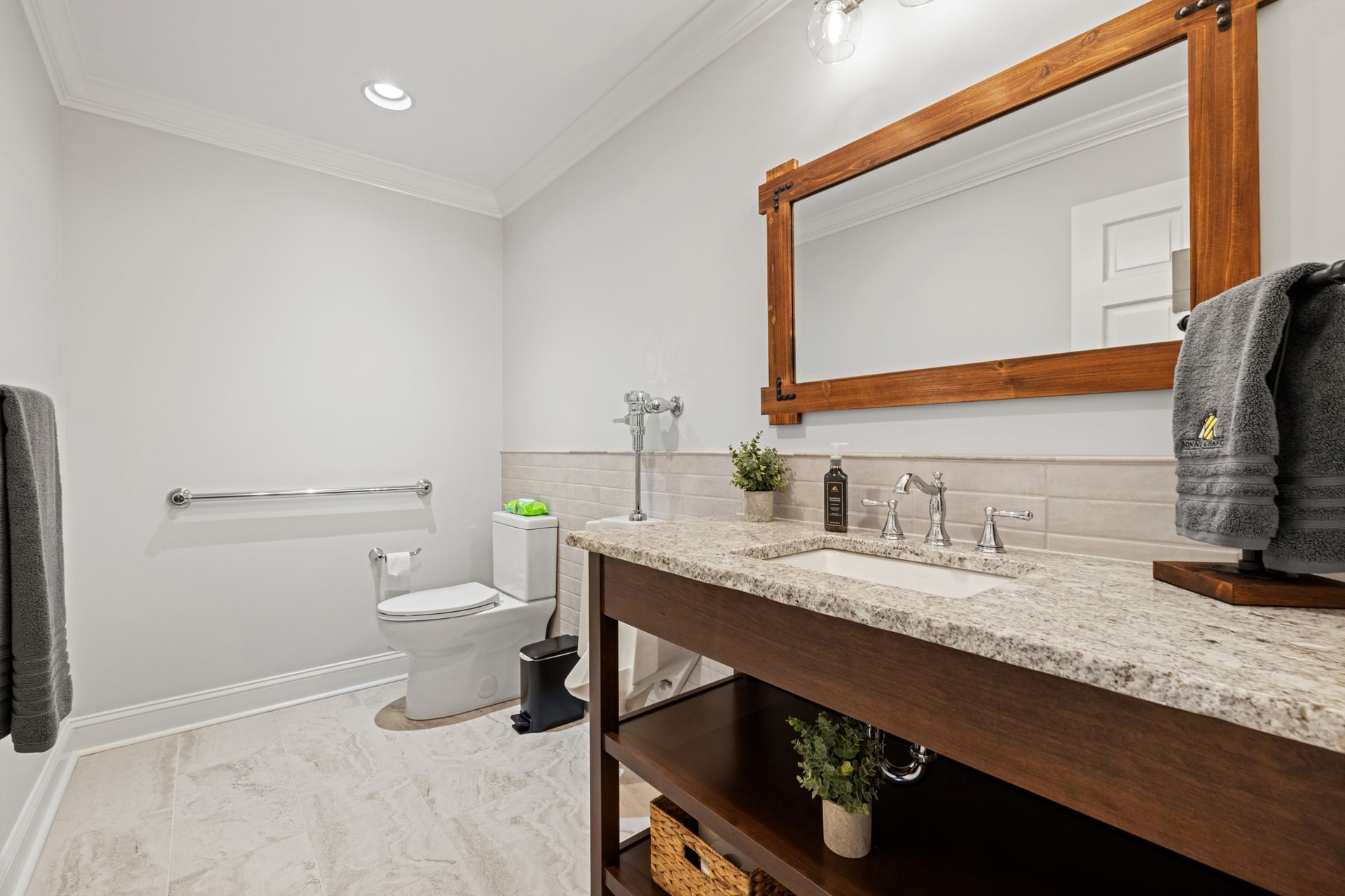 Bathroom with wooden vanity, granite countertop, large mirror, and toilet.