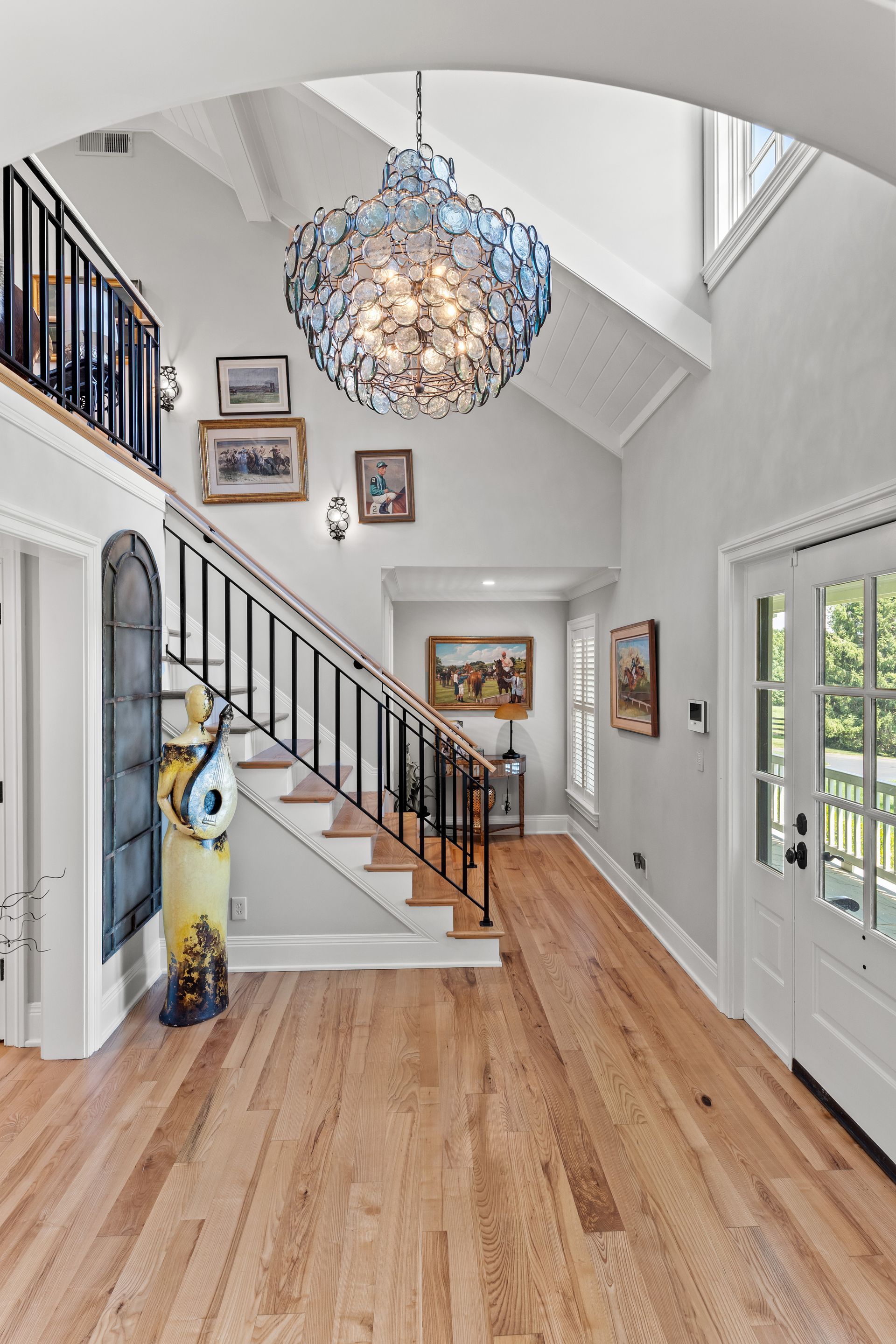 Elegant foyer with a grand staircase, light wood floors, and a large chandelier.