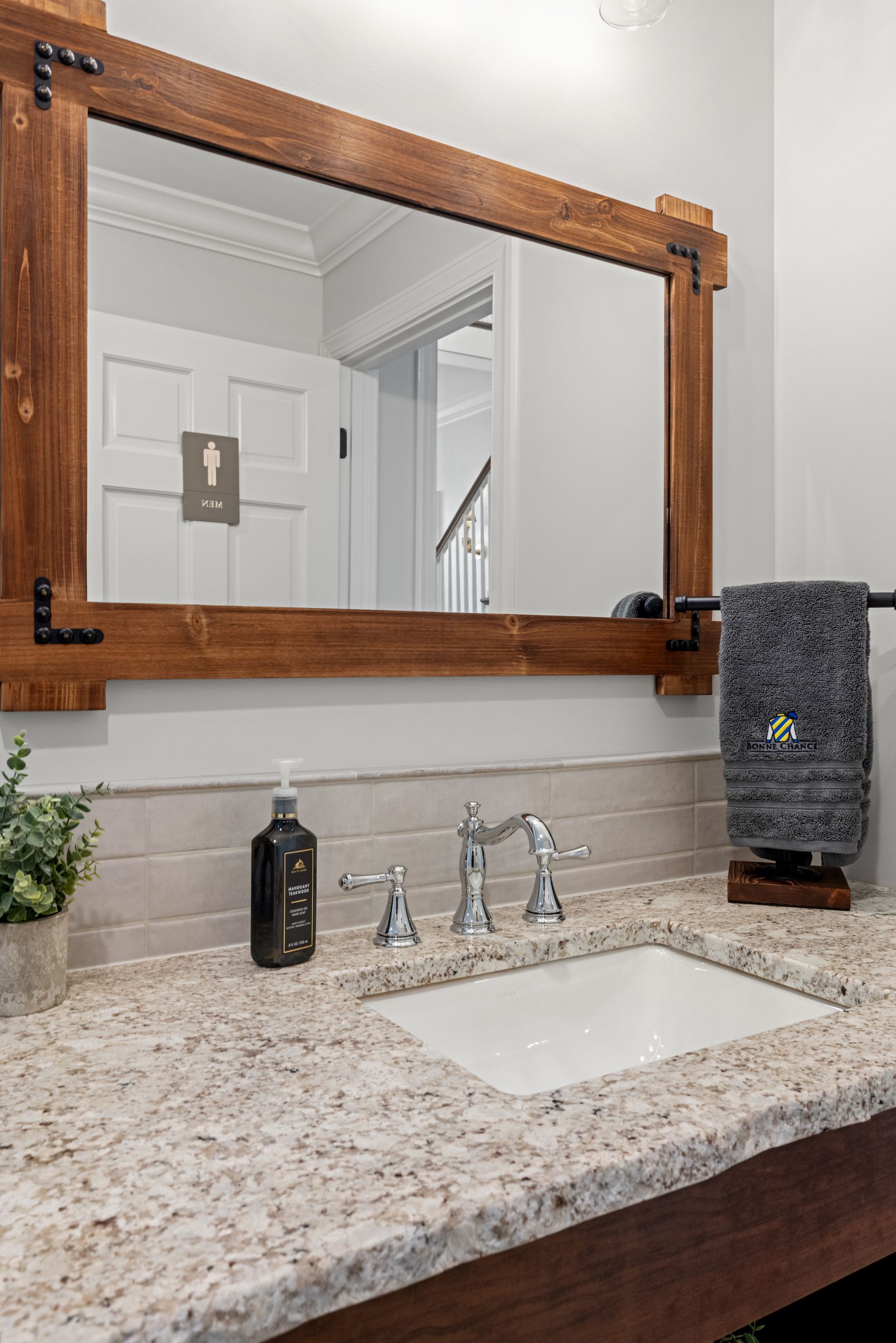 Bathroom with a wood-framed mirror, granite countertop, and silver faucet. Gray towel and soap dispenser.
