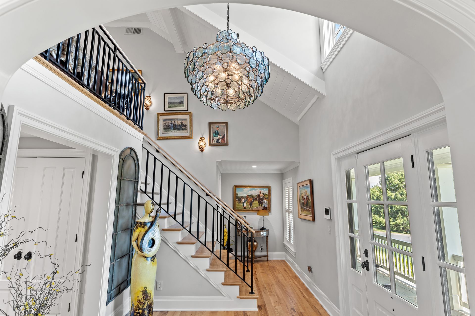Bright white entry with staircase, blue chandelier, and artwork.