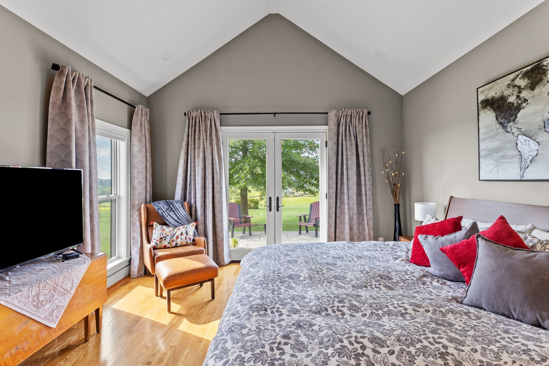 Bedroom with a large bed, arm chair, and doors leading to a patio and a grassy yard.