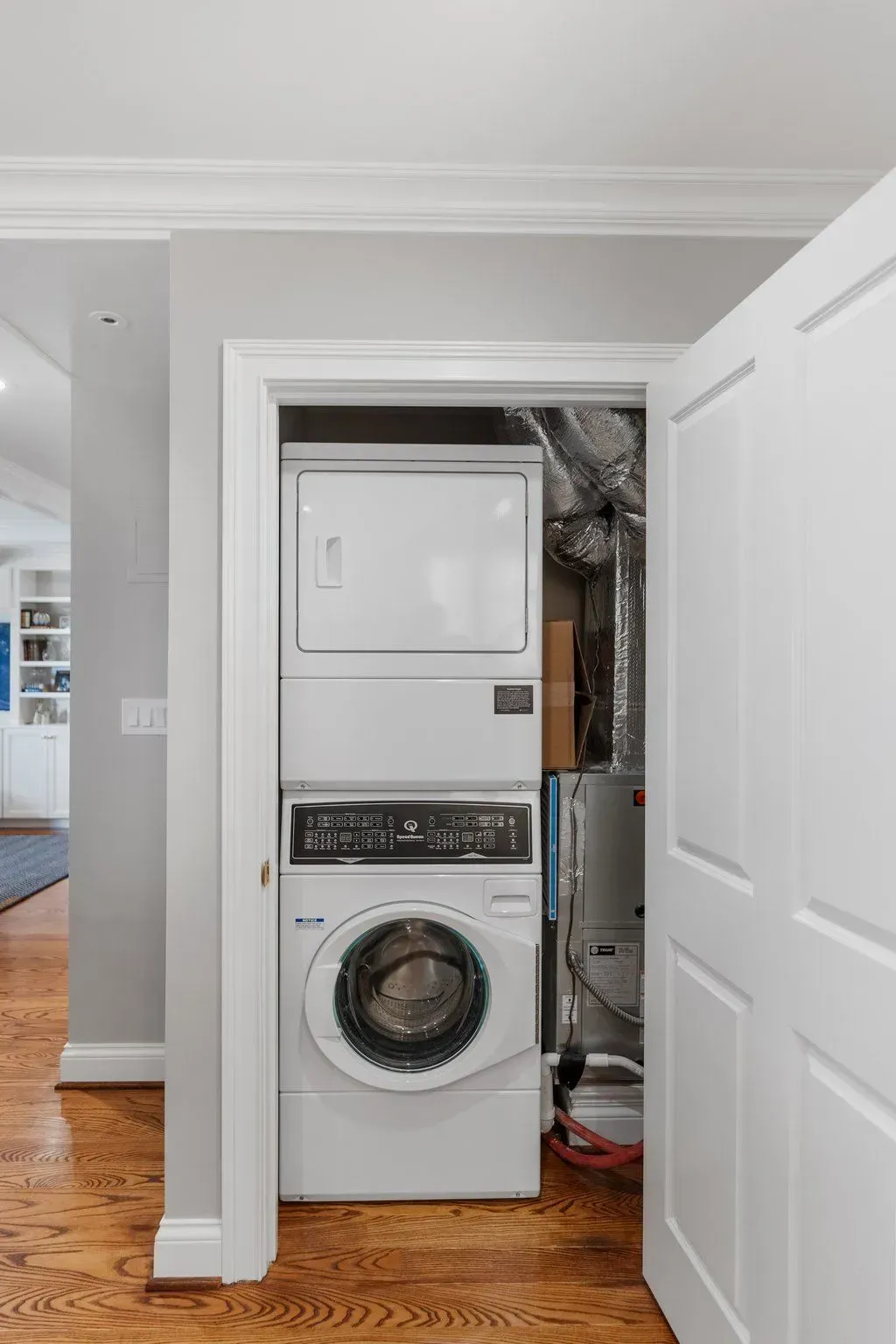 Stackable washer and dryer in a closet with hardwood floors. White appliances, grey walls, and open door.