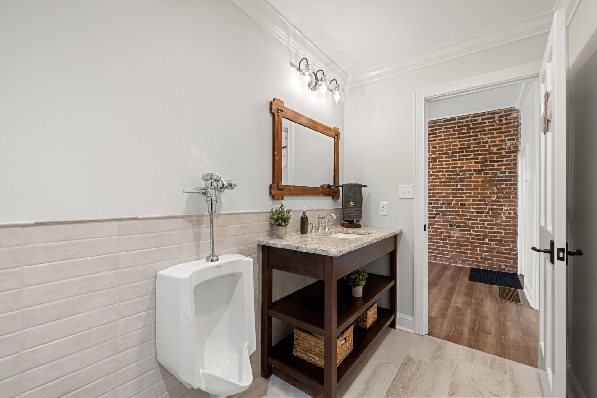 Bathroom with a urinal, vanity, and brick accent wall.