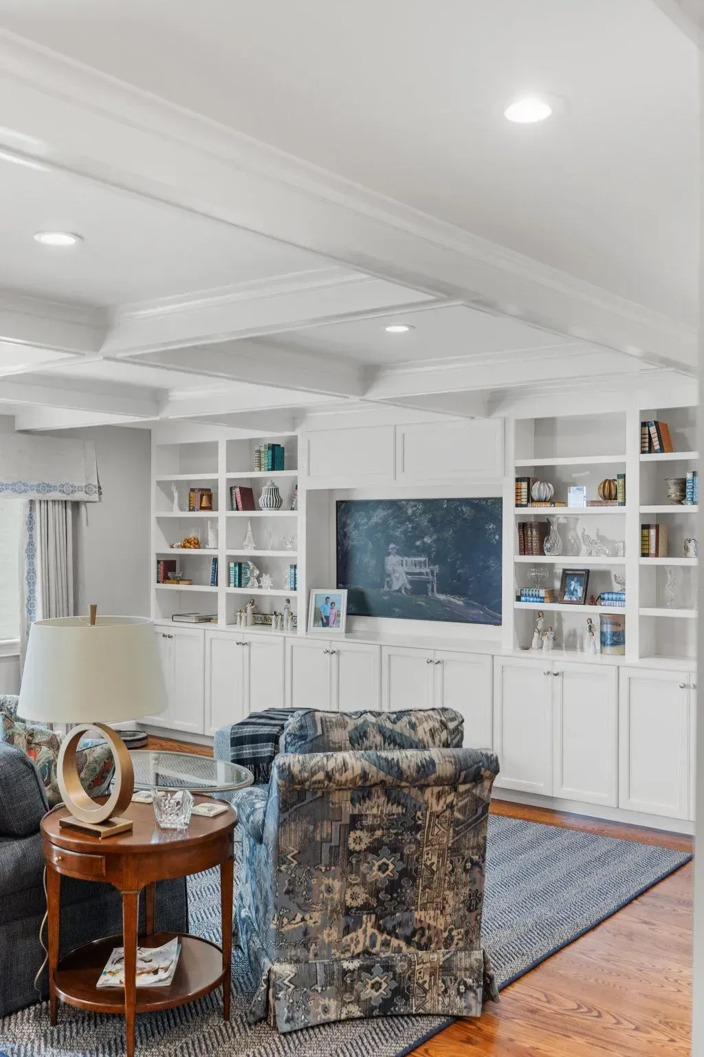 Living room with built-in white shelving, TV, two patterned armchairs, and a wooden side table.