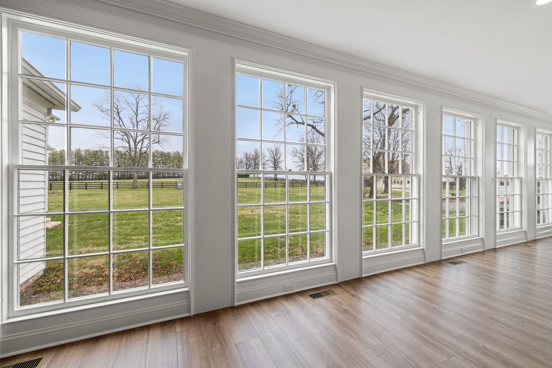 Row of white-framed windows looking out onto a green field, with a hardwood floor inside.