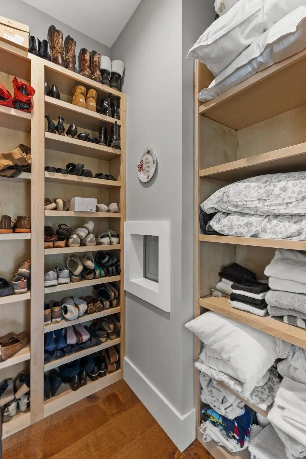 Walk-in closet with shoe shelves on one side and linen shelves on the other; gray walls, light wood shelving.