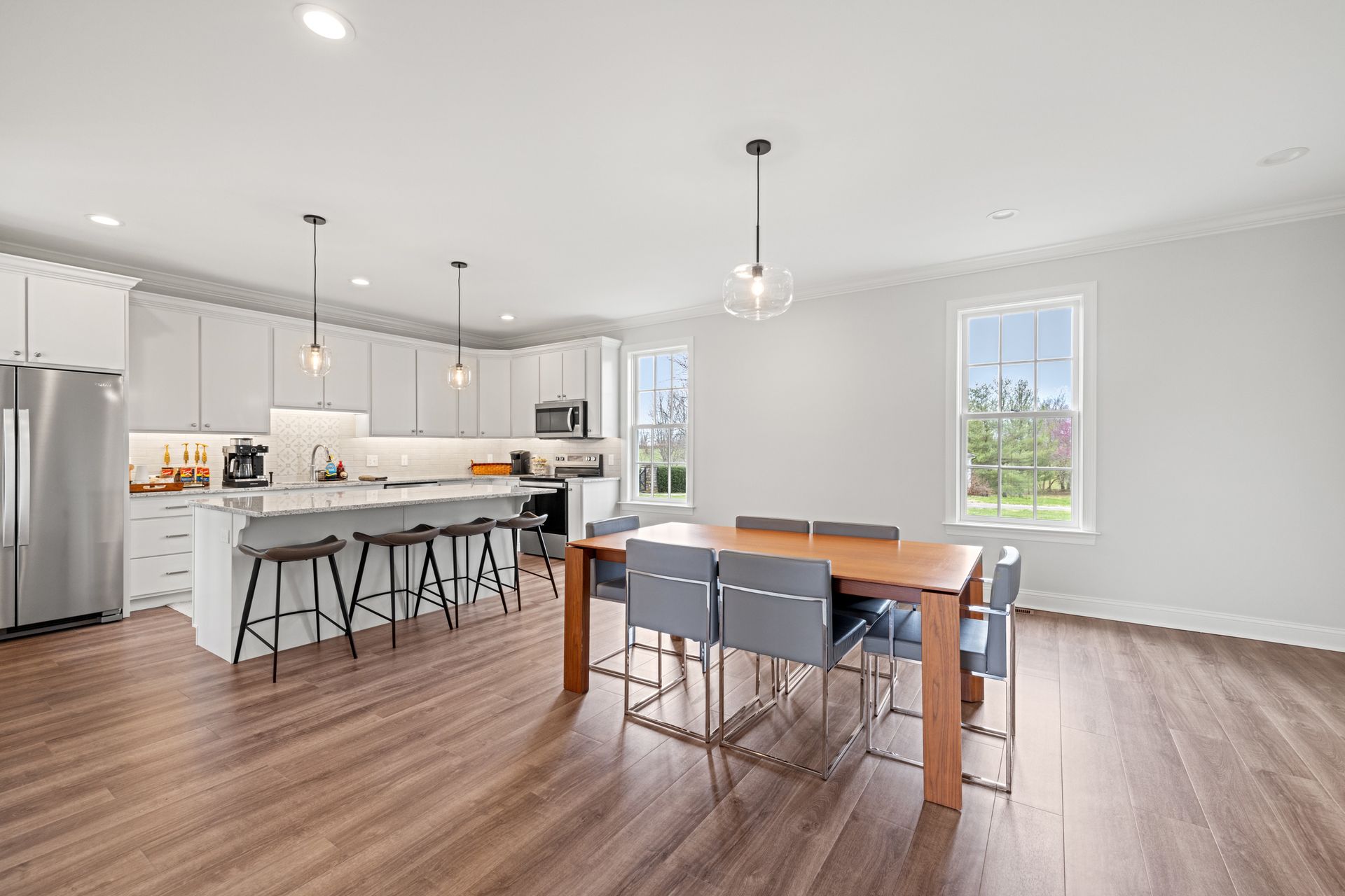 Spacious modern kitchen with white cabinets, island, and wooden floor; dining table with chairs.