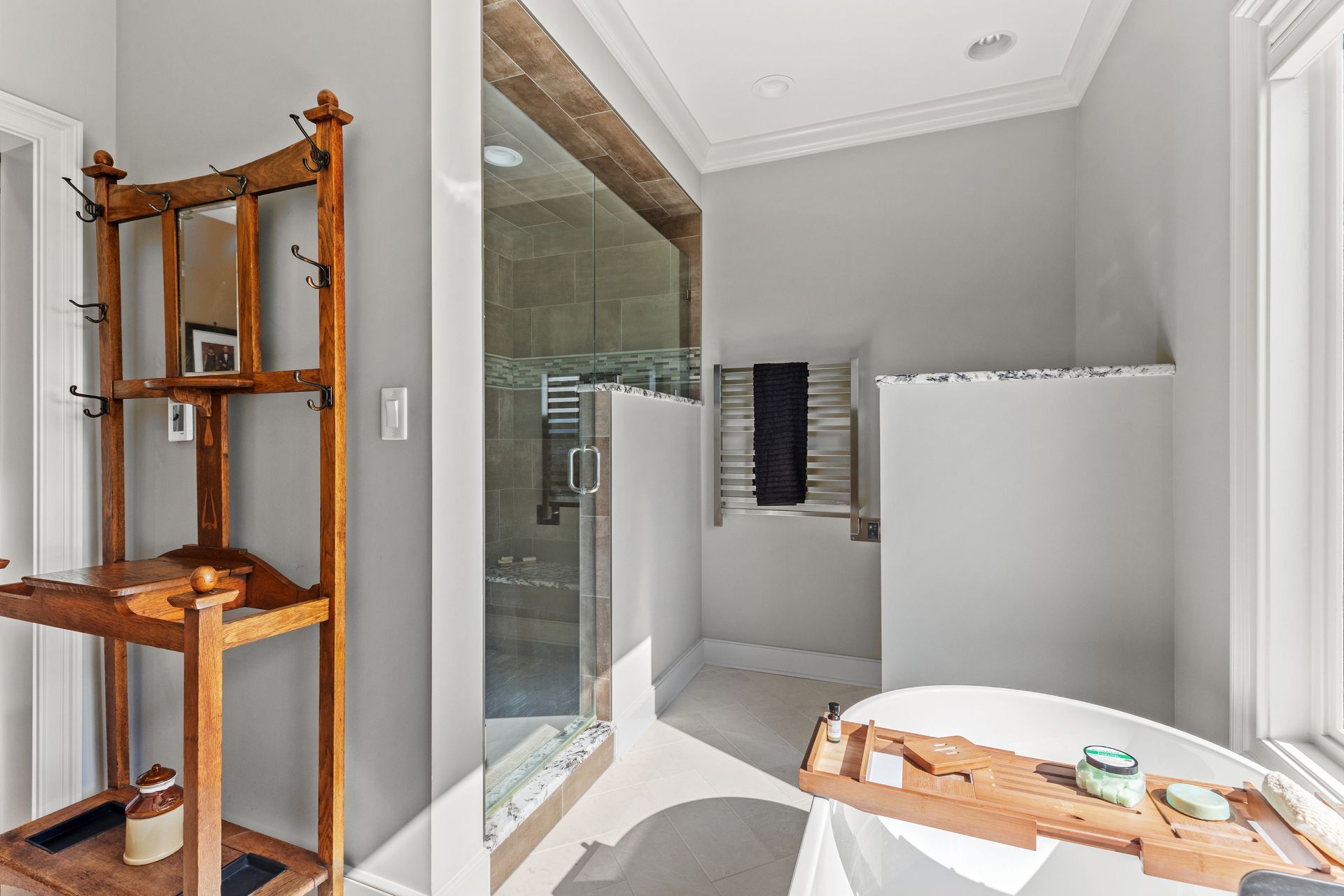 Bathroom with a glass shower, wooden shelf, and freestanding tub; gray walls.