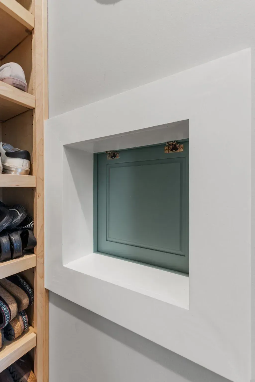 Built-in wall niche with a teal-colored door inside a white frame, beside shoe shelves.
