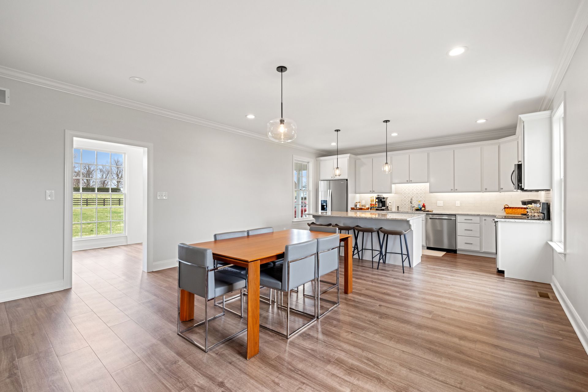 Open-concept kitchen with wooden floor, dining table and chairs, and a bright window.