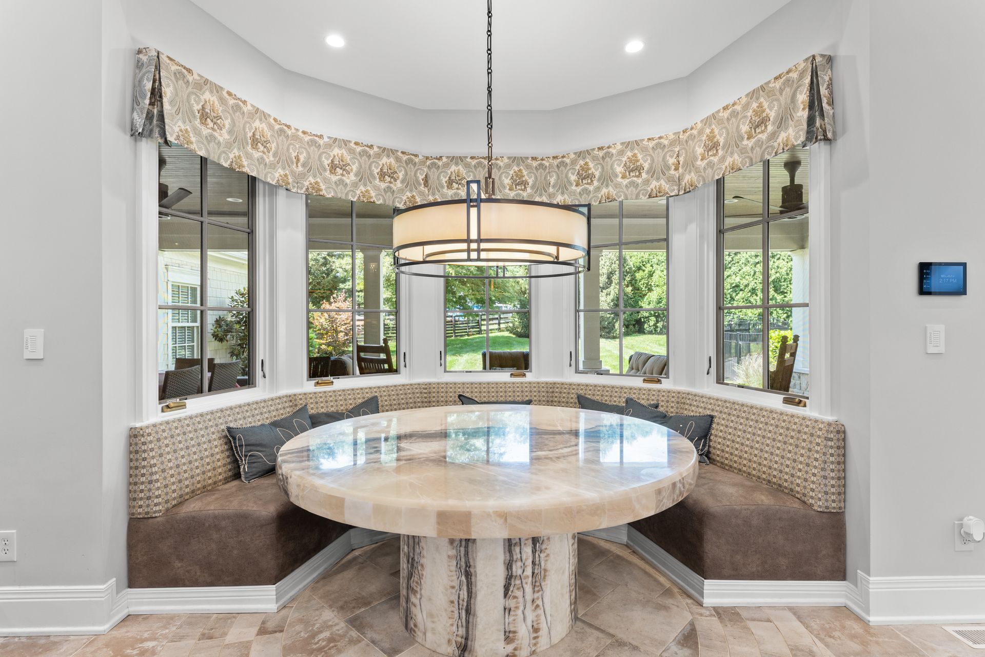 A round dining table and built-in bench in a curved bay window area with a large pendant light.
