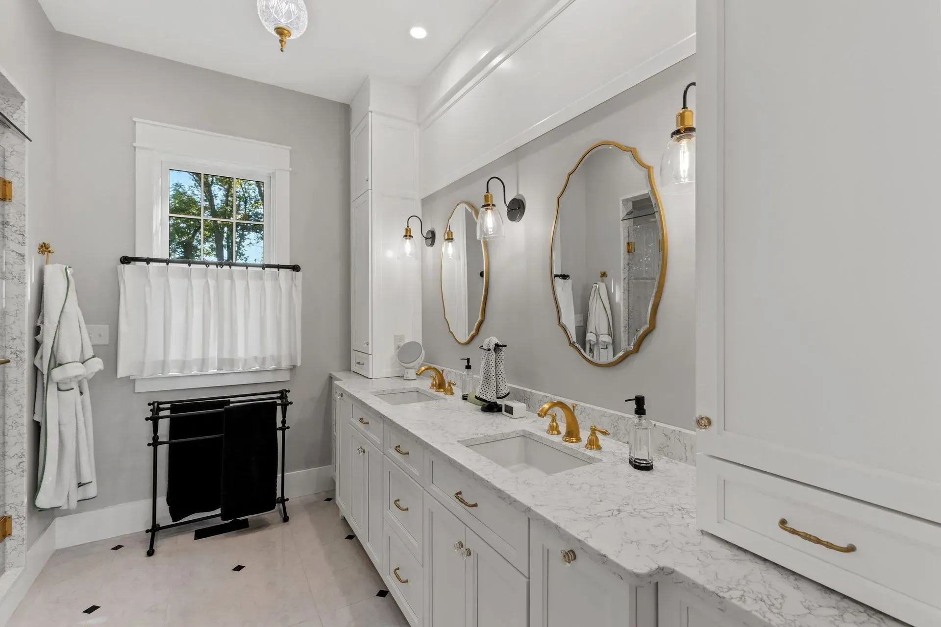 Elegant white bathroom with double vanity, gold accents, and a window.