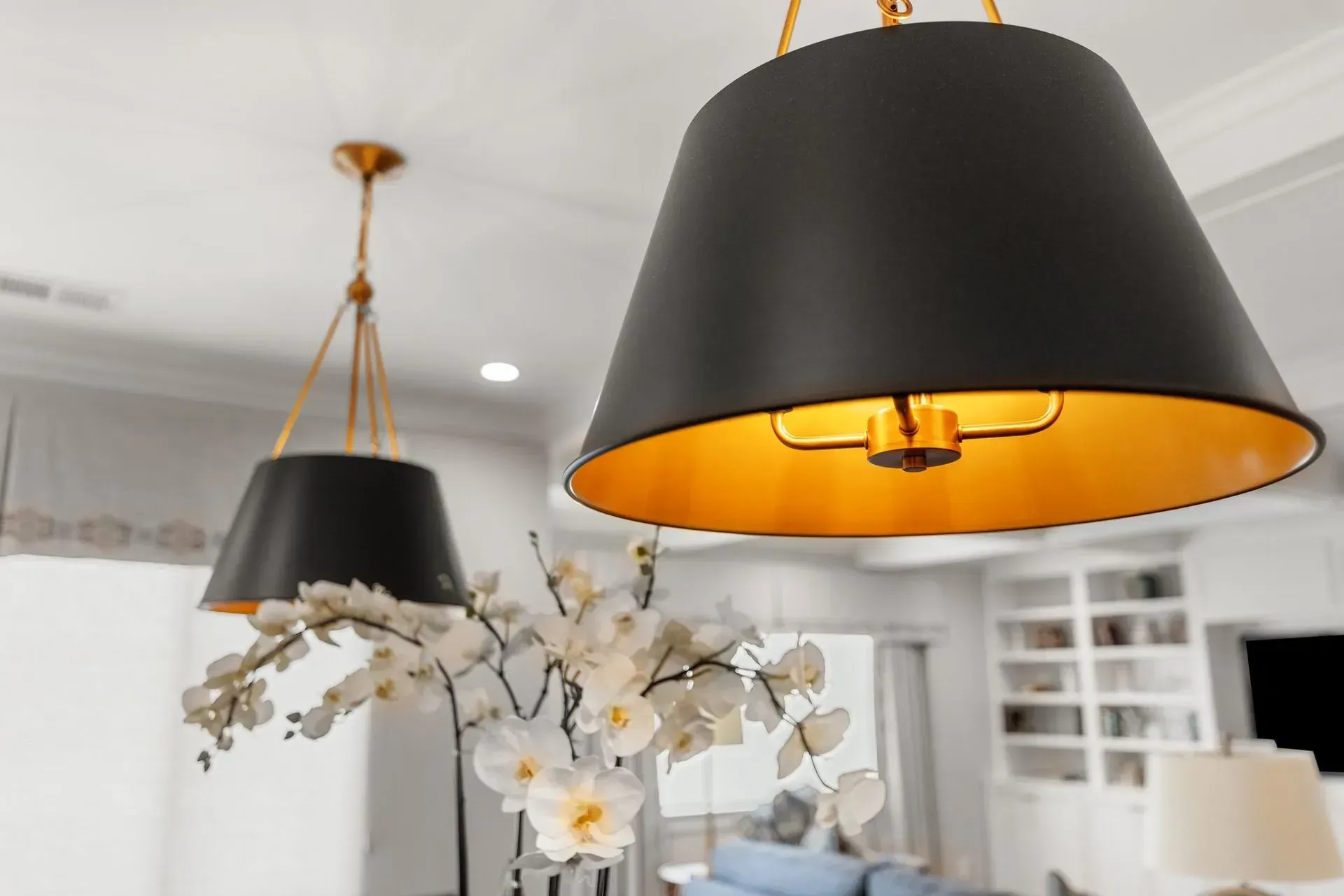 Two black and gold pendant lights hanging above a white flower arrangement in a home.