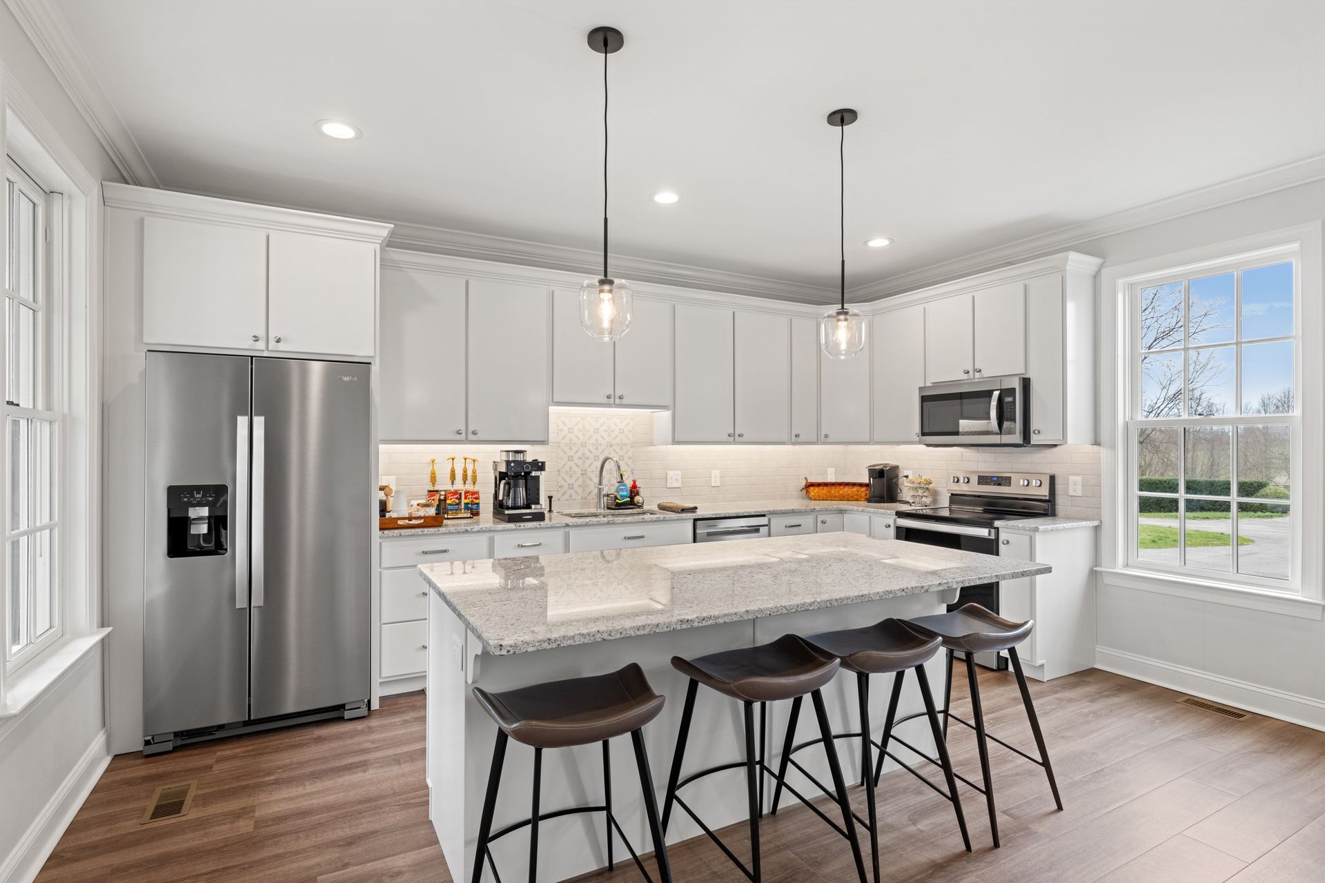 Bright, modern kitchen with white cabinets, stainless steel appliances, and a granite countertop island with stools.