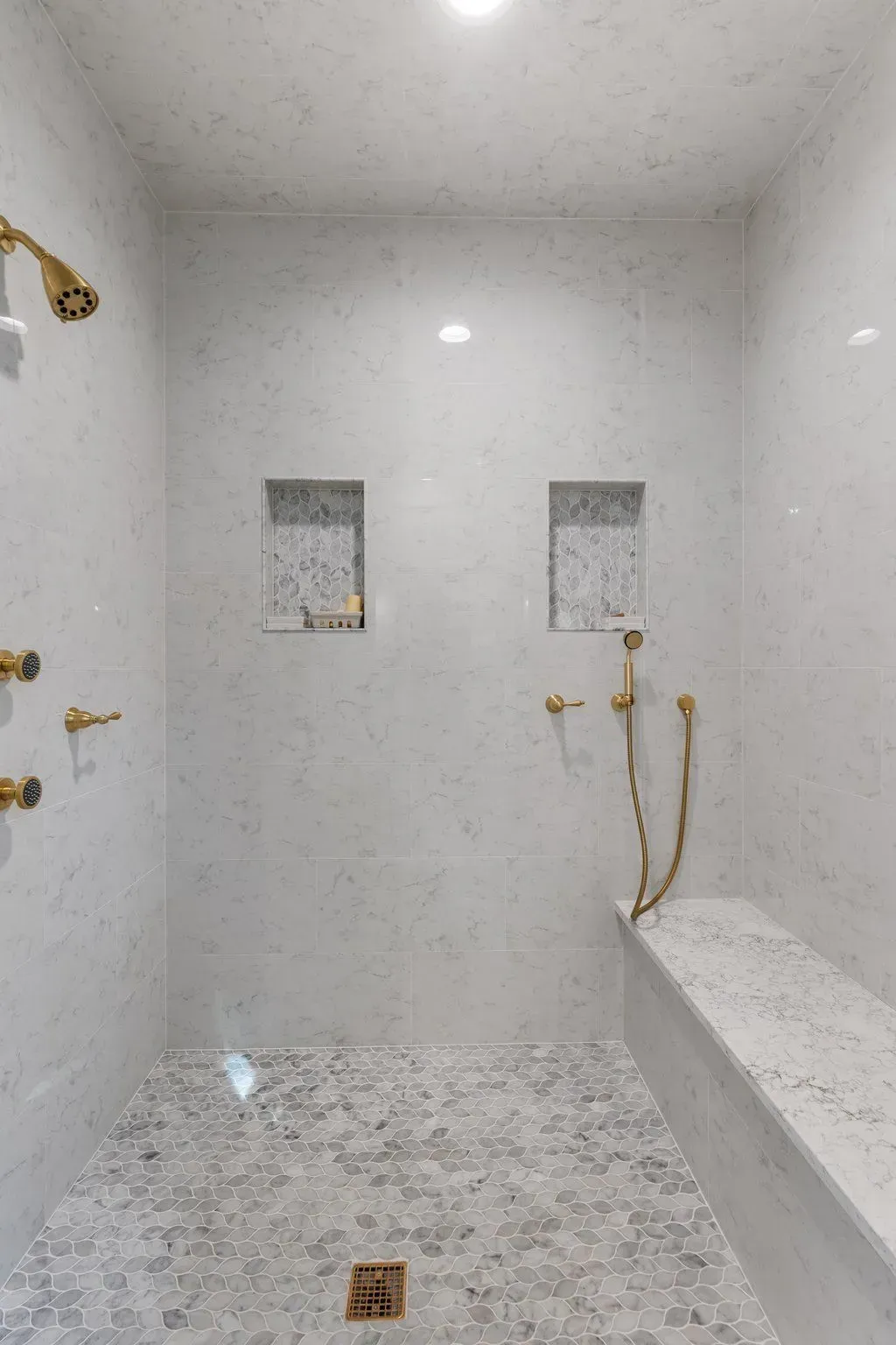 Luxurious white marble shower with gold fixtures, built-in bench, and mosaic floor.