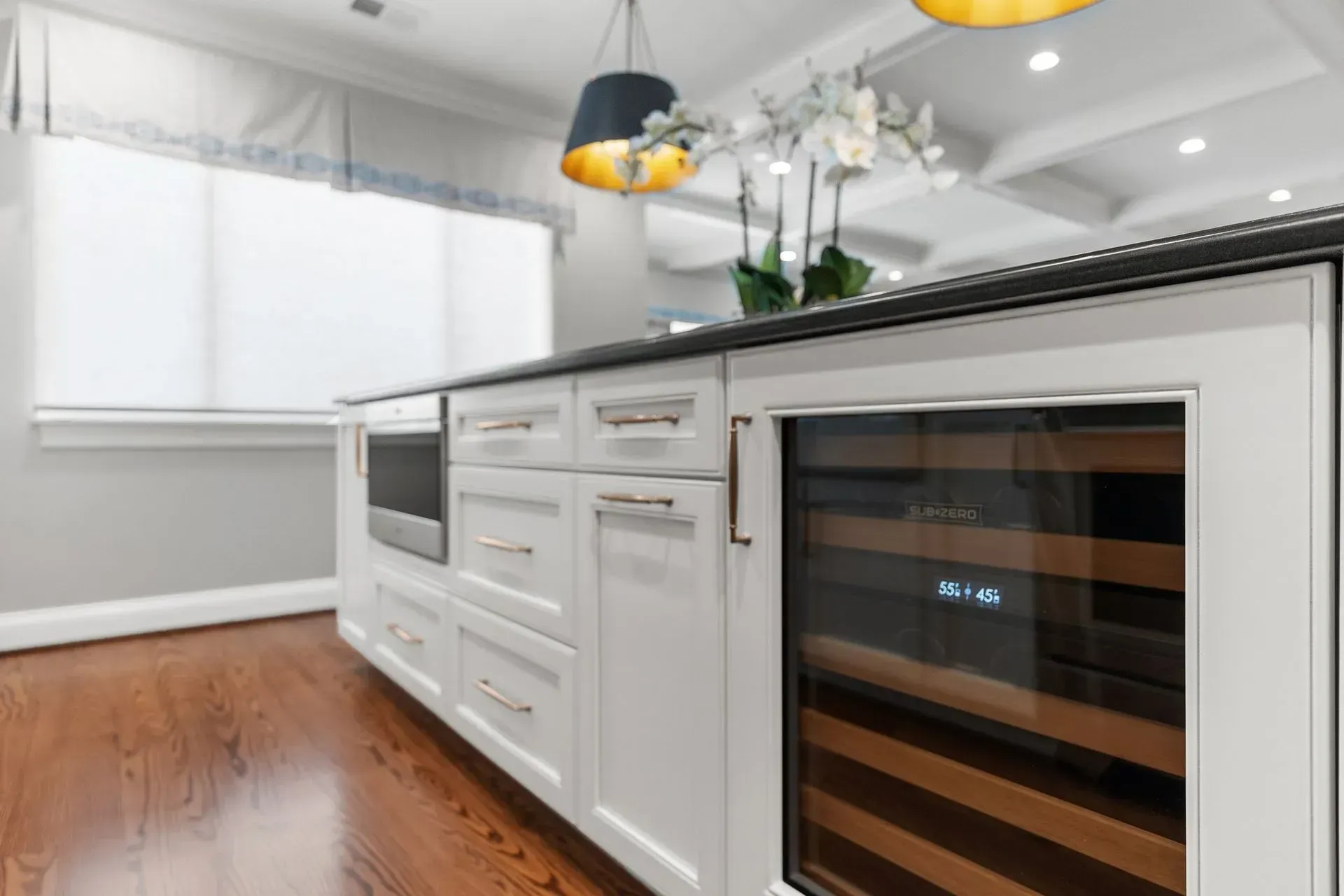 White kitchen island with built-in wine fridge, drawers, and microwave on dark wood floor.