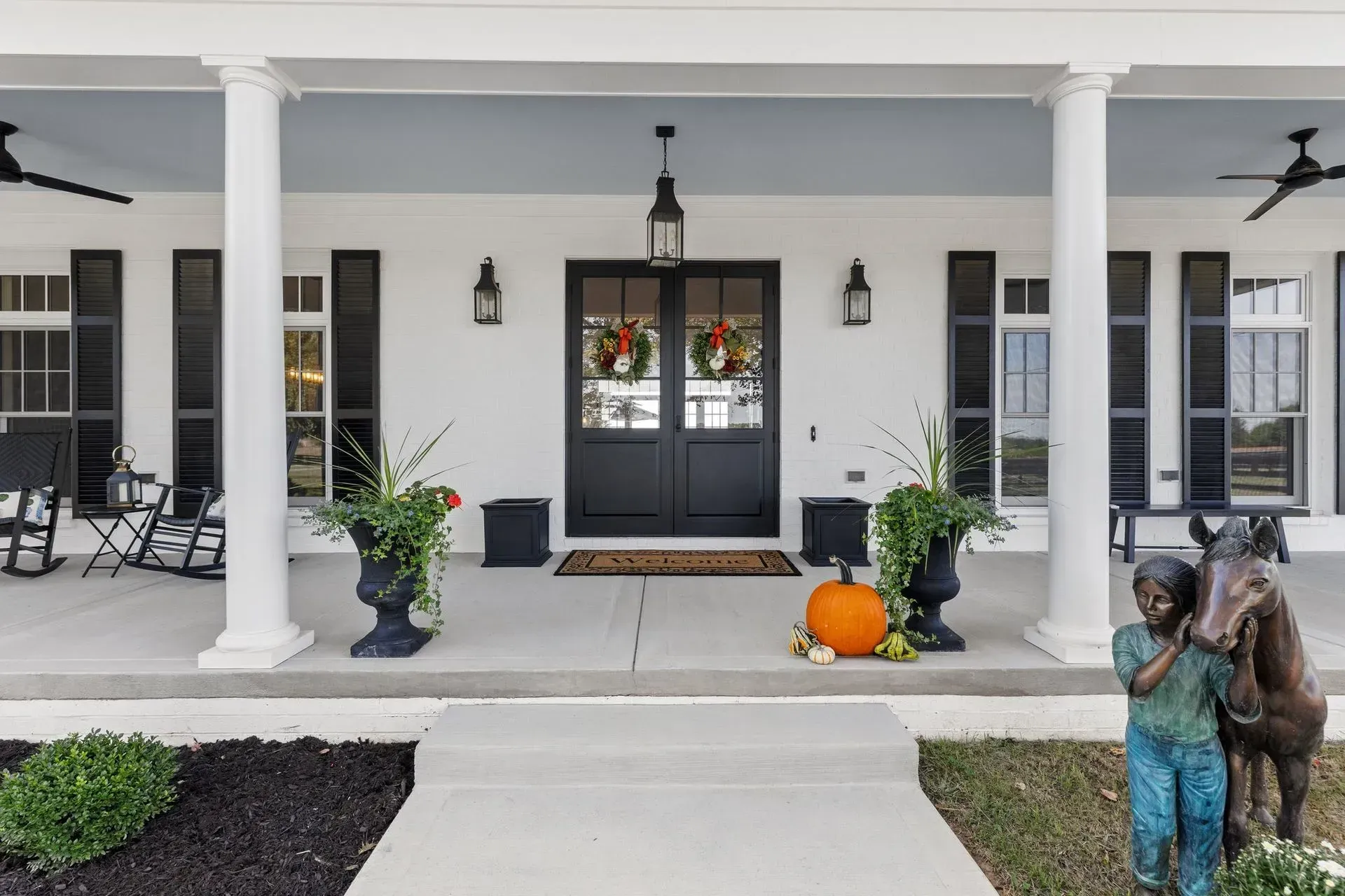 White farmhouse entrance with black doors, shutters, and accents; fall decor.