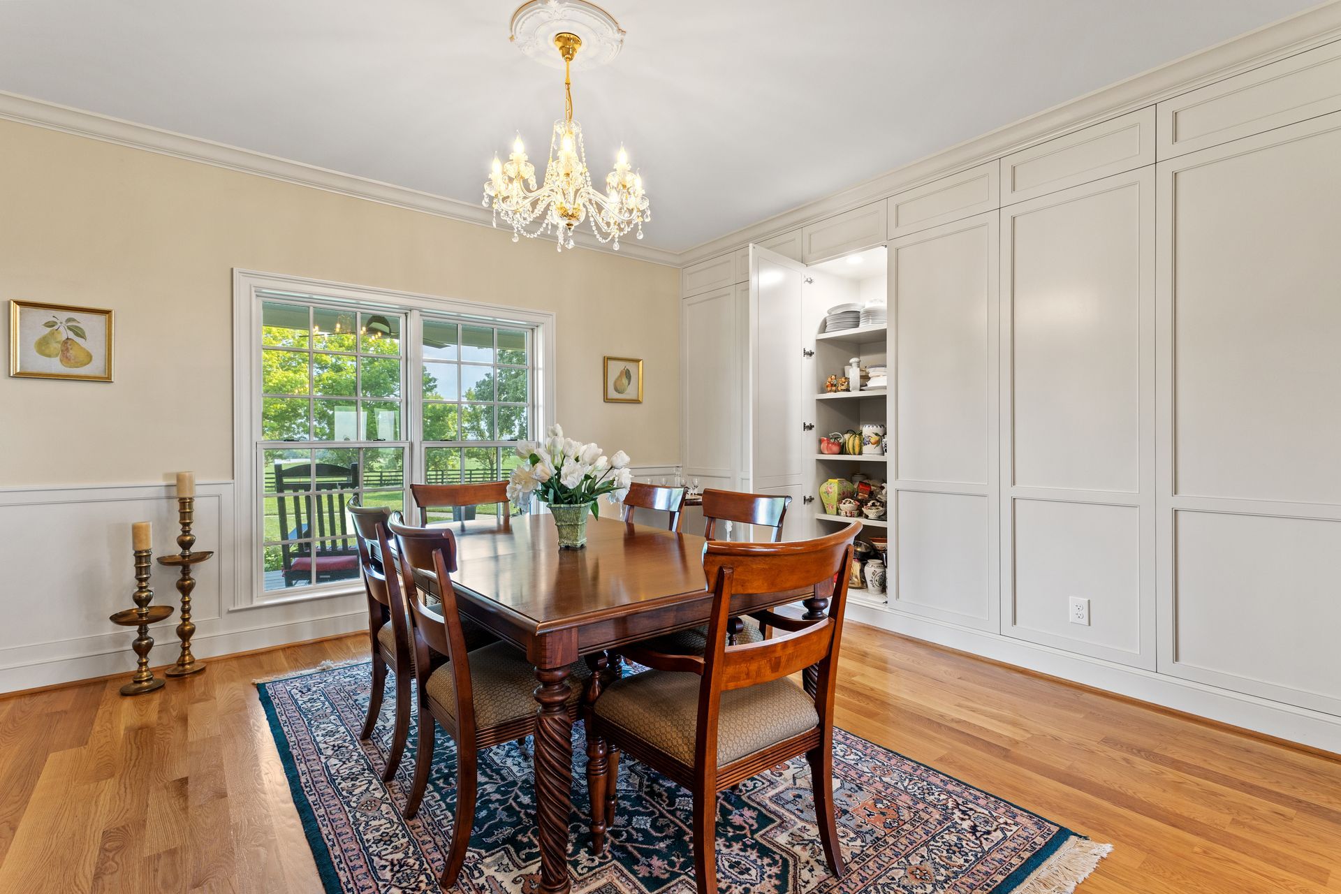 Formal dining room with wooden table, chairs, and chandelier; built-in pantry and outside view.