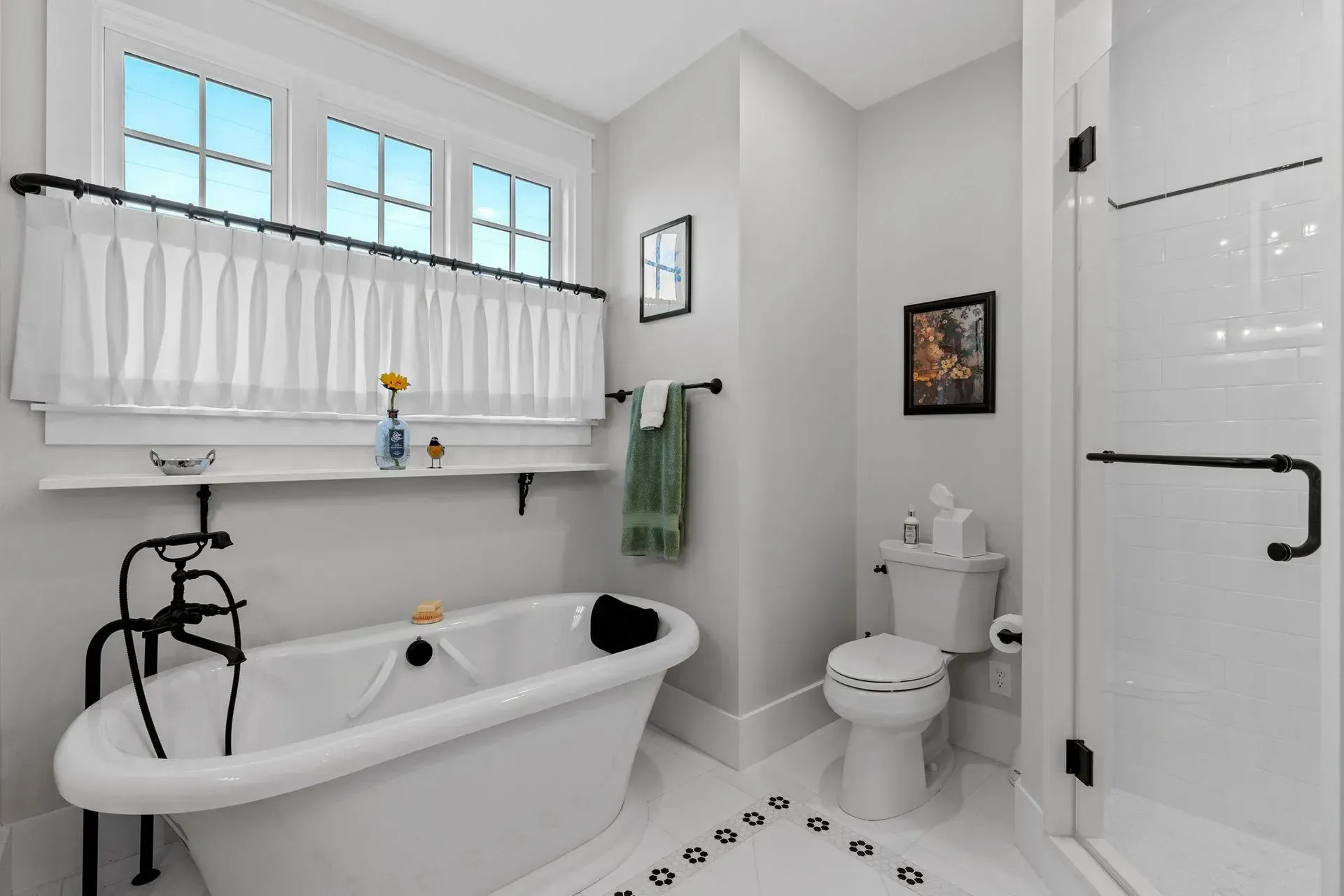Bathroom with white tub, shower, toilet, and light gray walls; window with sheer curtain.