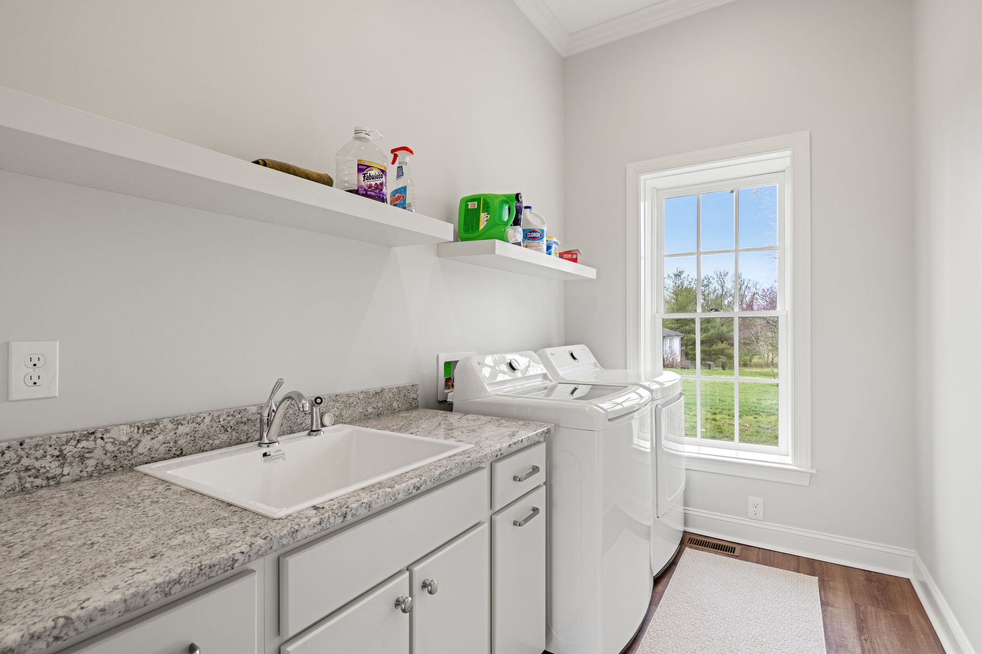 Laundry room with a sink, washer, and dryer, along with supplies on shelves near a window.