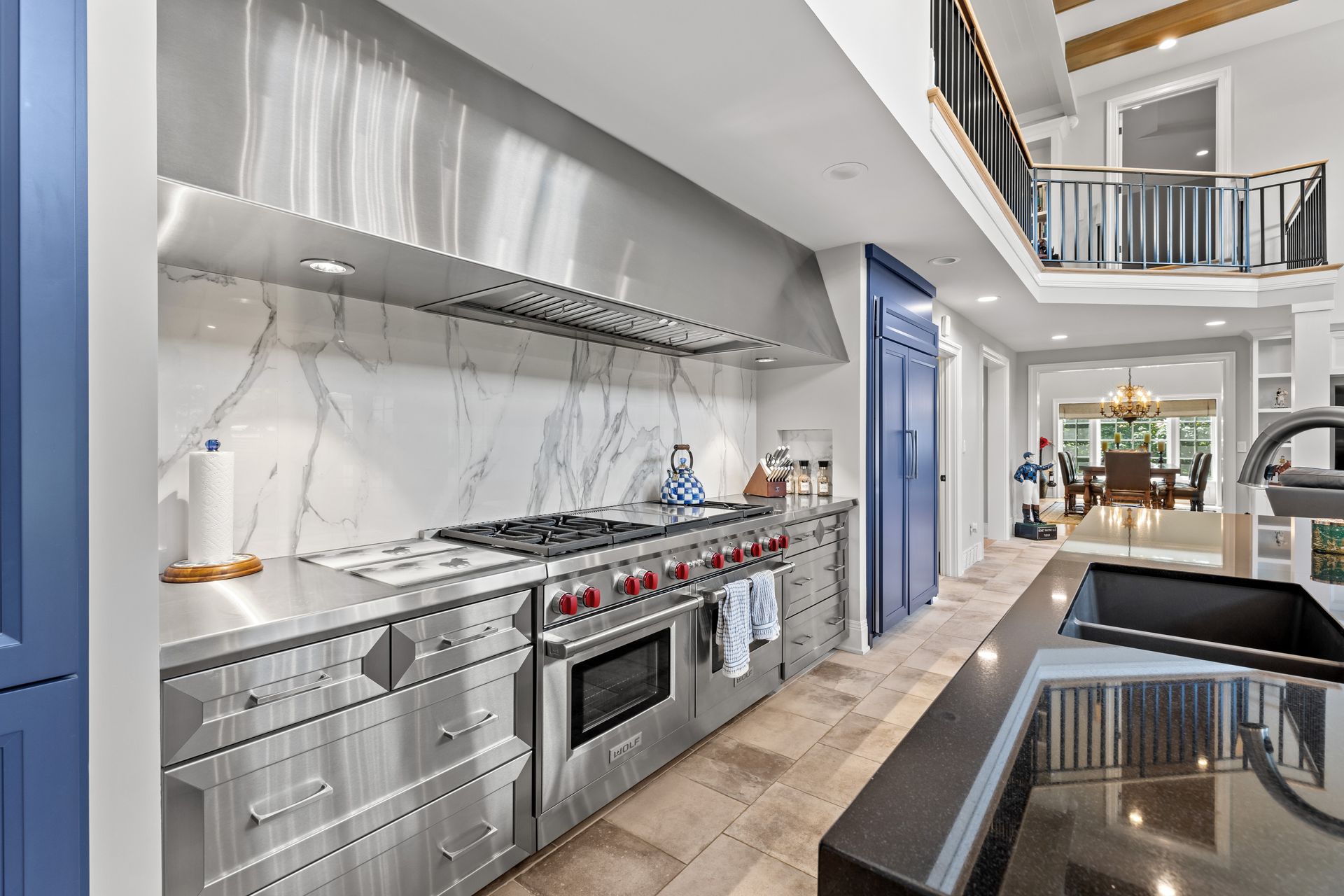 Stainless steel kitchen with a marble backsplash, blue accents, and a view of a dining area.