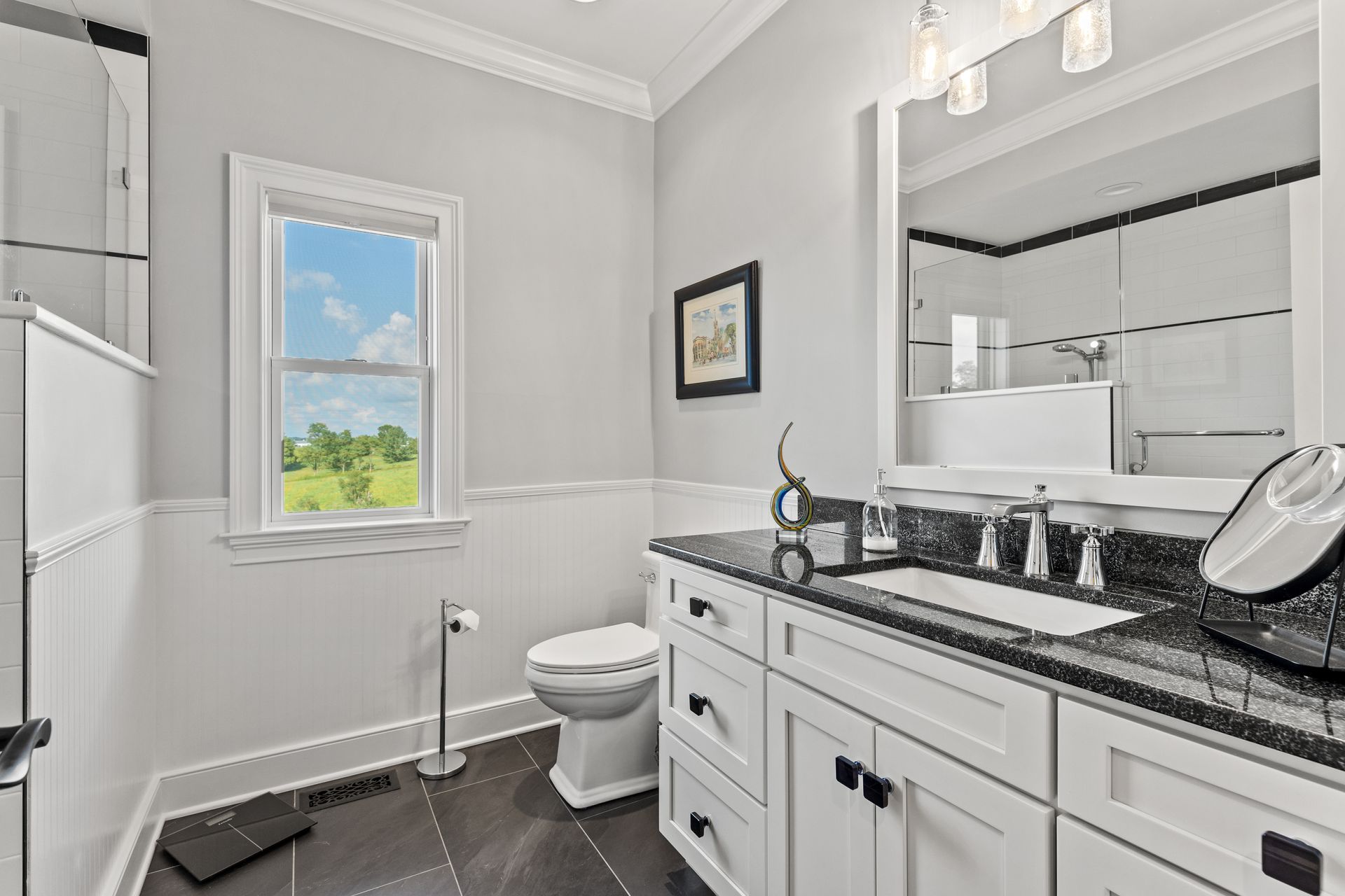 Bright bathroom with white cabinets, black countertop, and a window with a view.