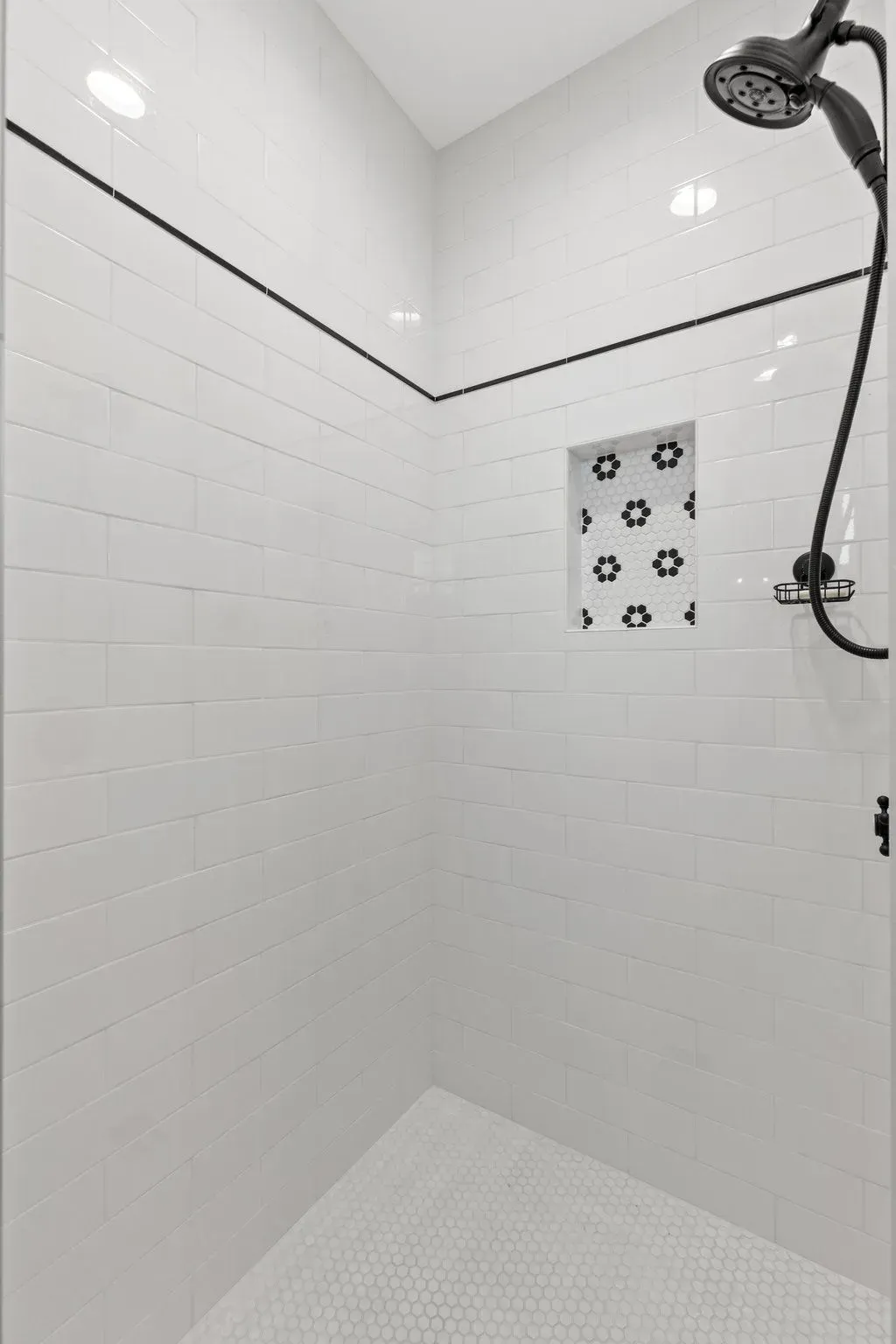 White tiled shower with black trim, a showerhead, and a built-in shelf.