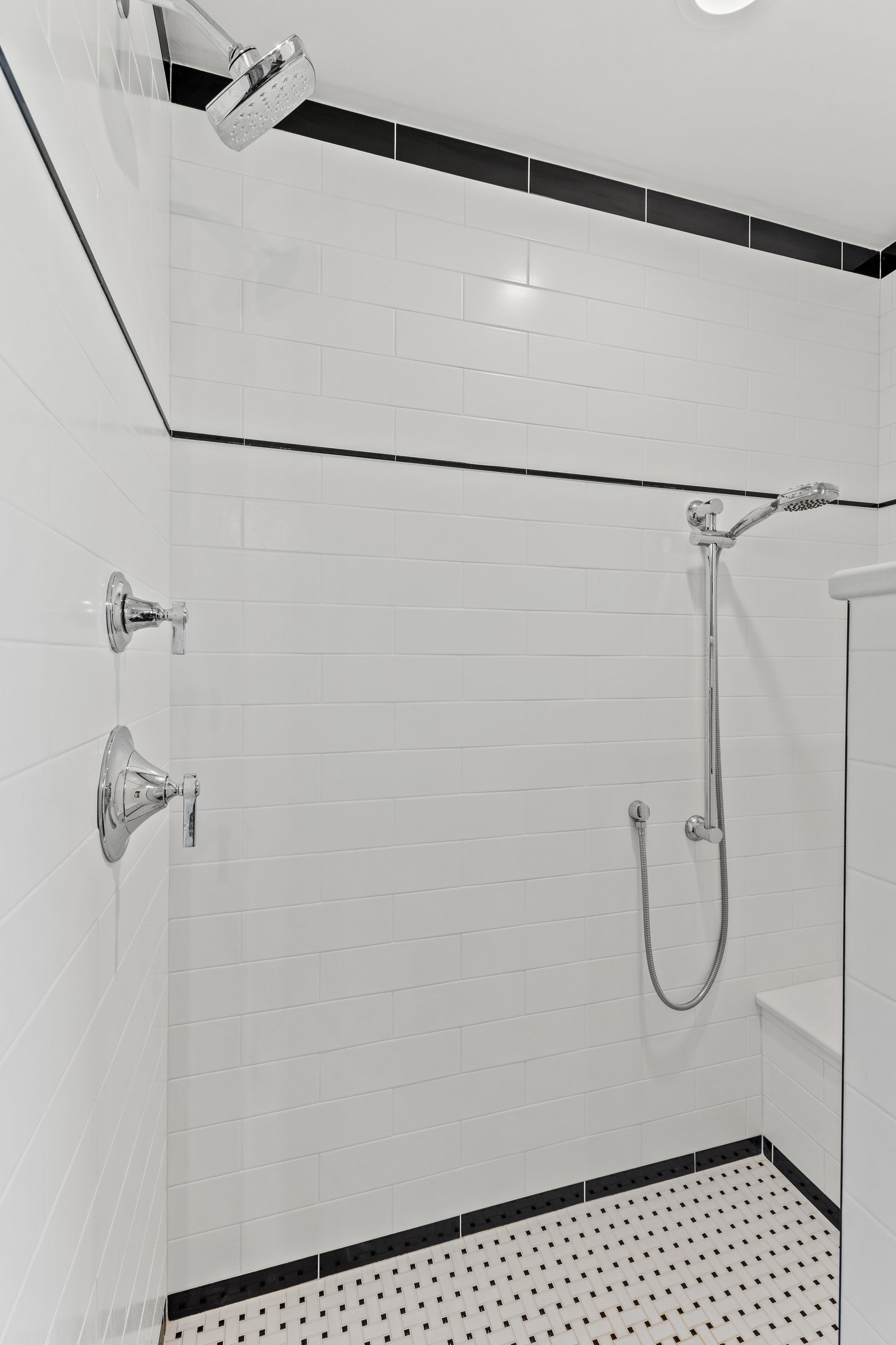 White tiled shower with black trim, silver fixtures, and penny tile floor.