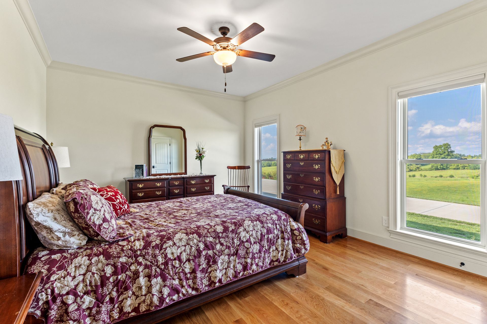 Bedroom with wooden furniture, floral bedding, and a view of a field.