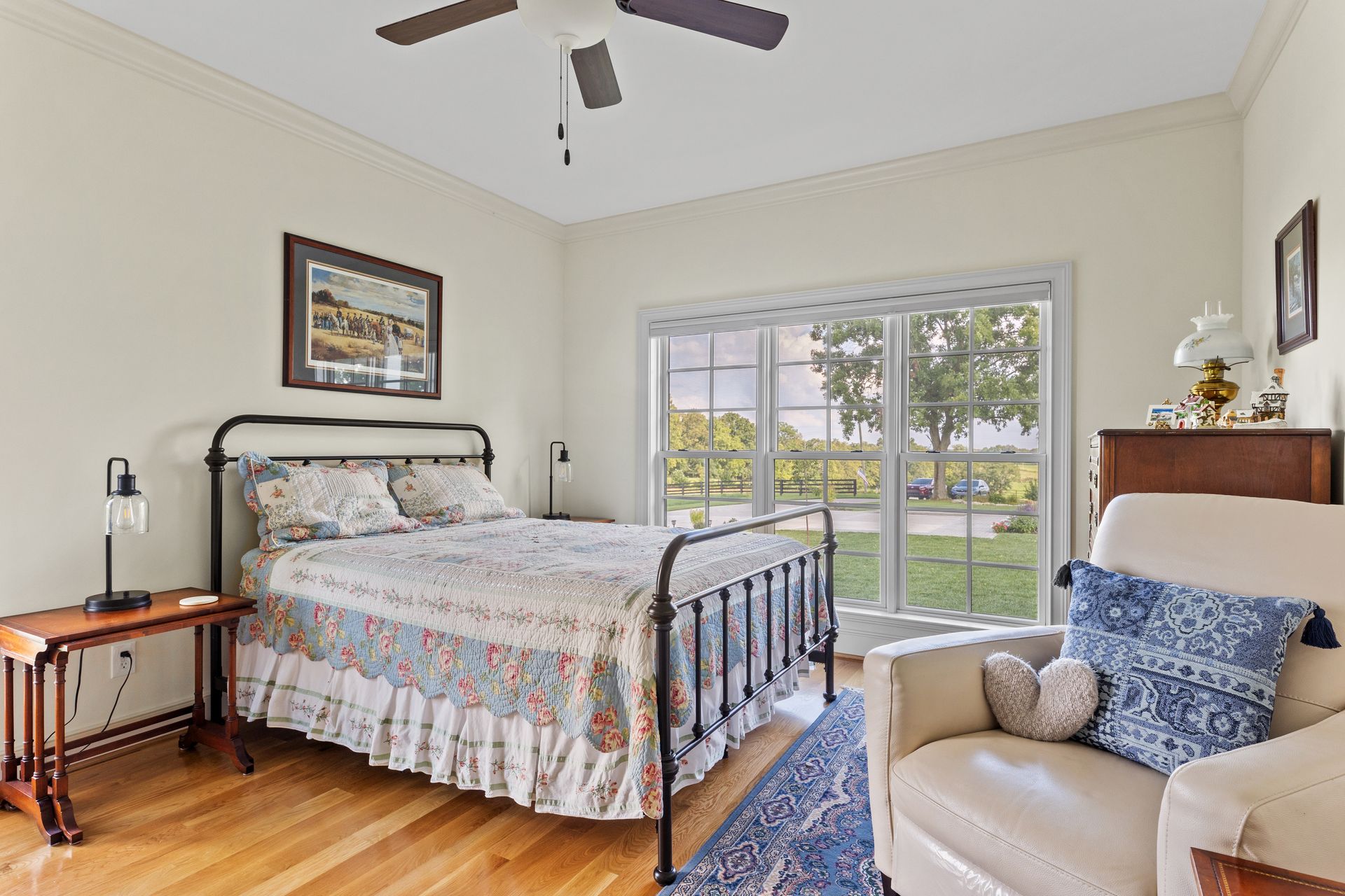 Bedroom with wrought iron bed, floral bedding, window, armchair, and wood furniture.