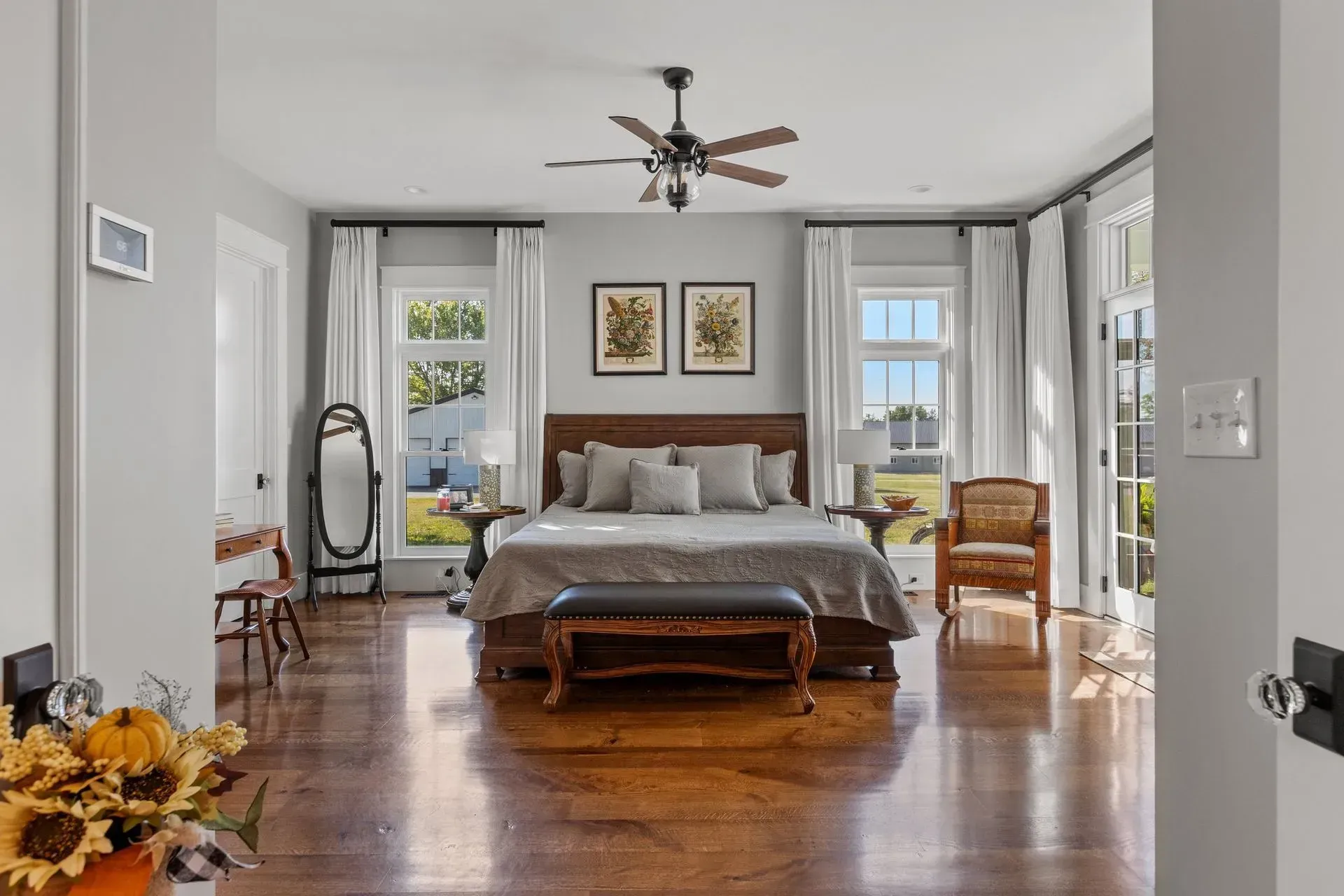 Spacious bedroom with a bed, wooden floor, windows, and furniture. Natural light fills the room.