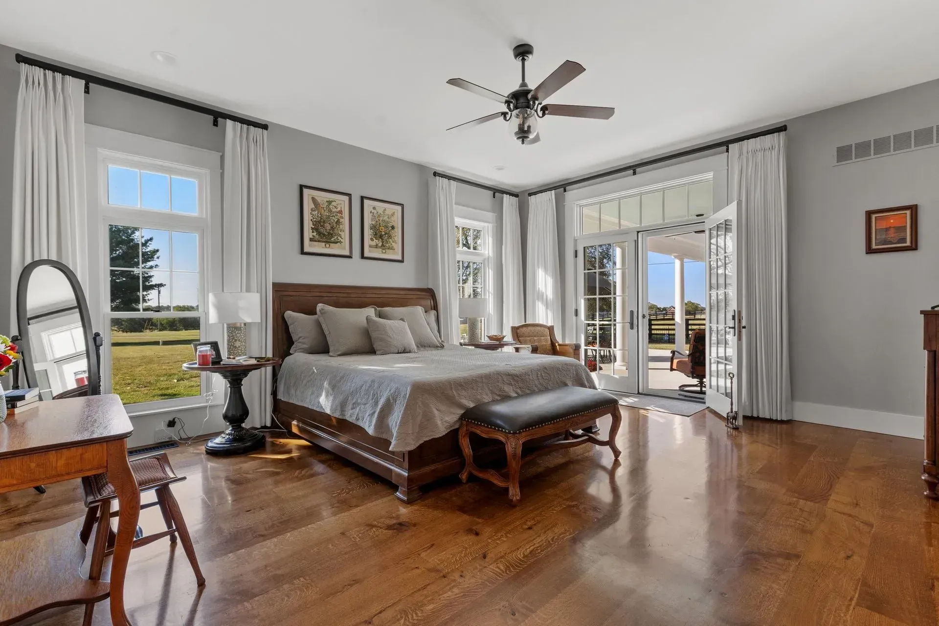 Spacious bedroom with hardwood floors, large windows, and bed facing French doors leading to a patio.