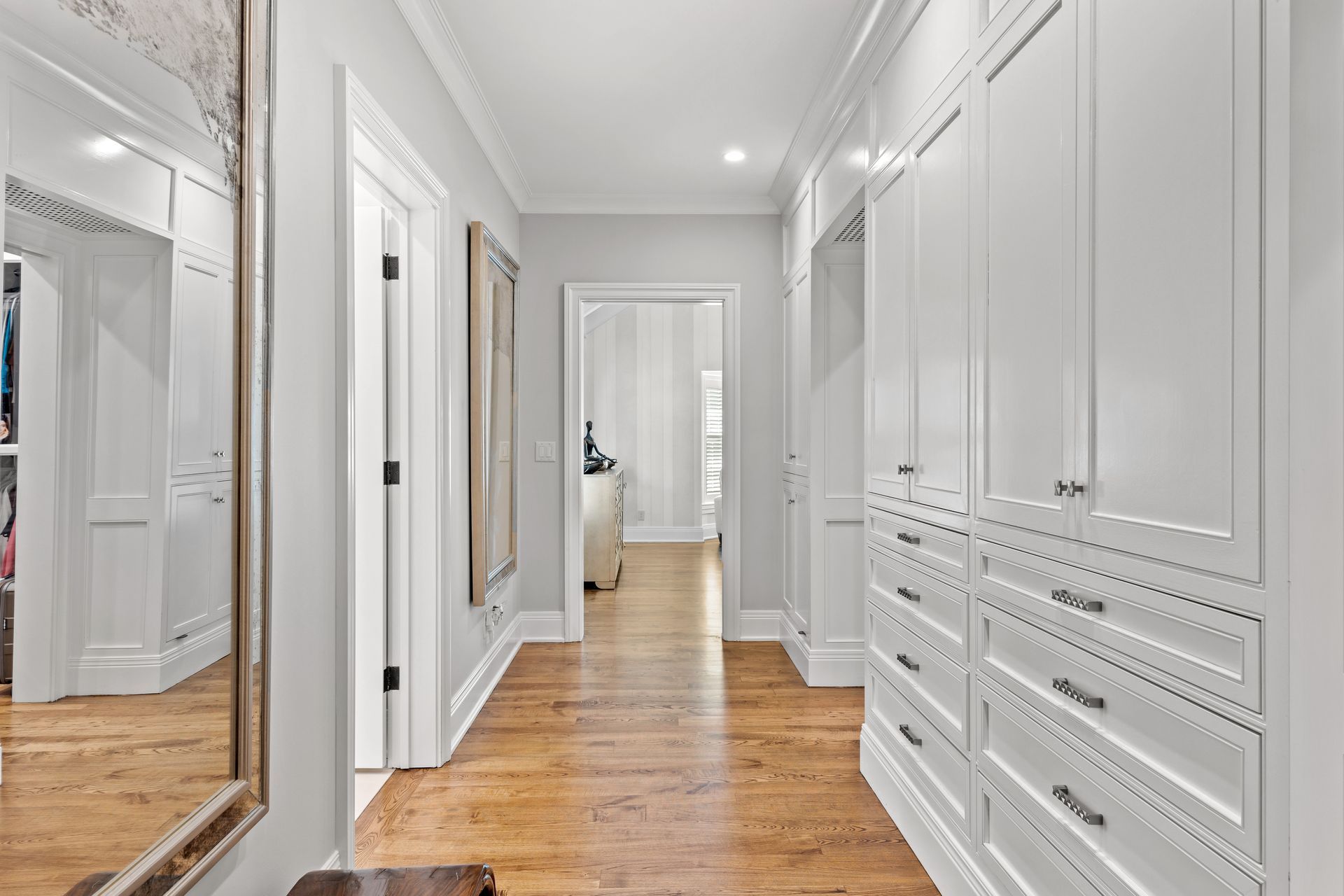 Long hallway with white built-in cabinets, hardwood floor, and a large mirror.