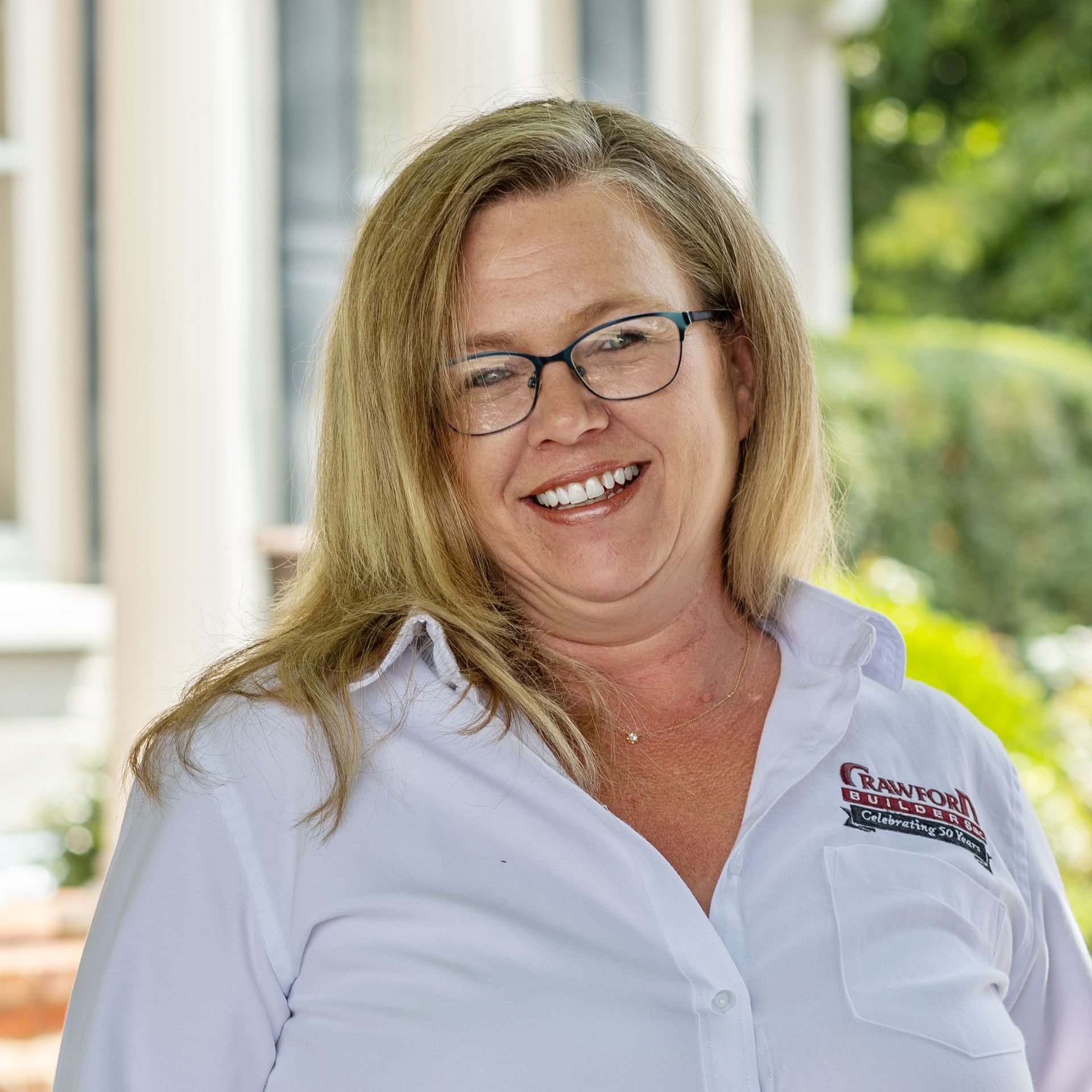 Woman with glasses and a white shirt smiles outdoors.