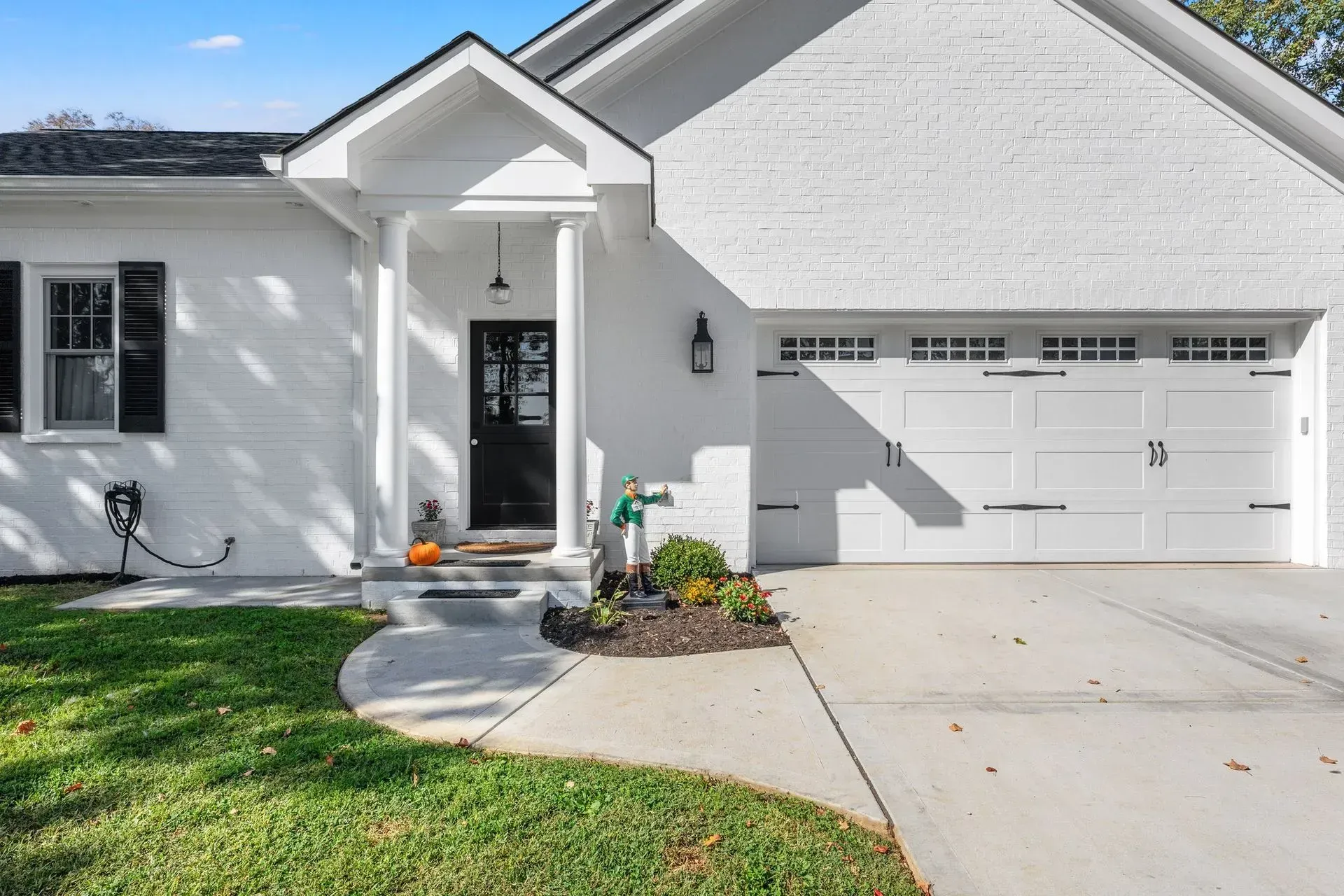 White-painted brick house with black front door and garage, black shutters, and green lawn.