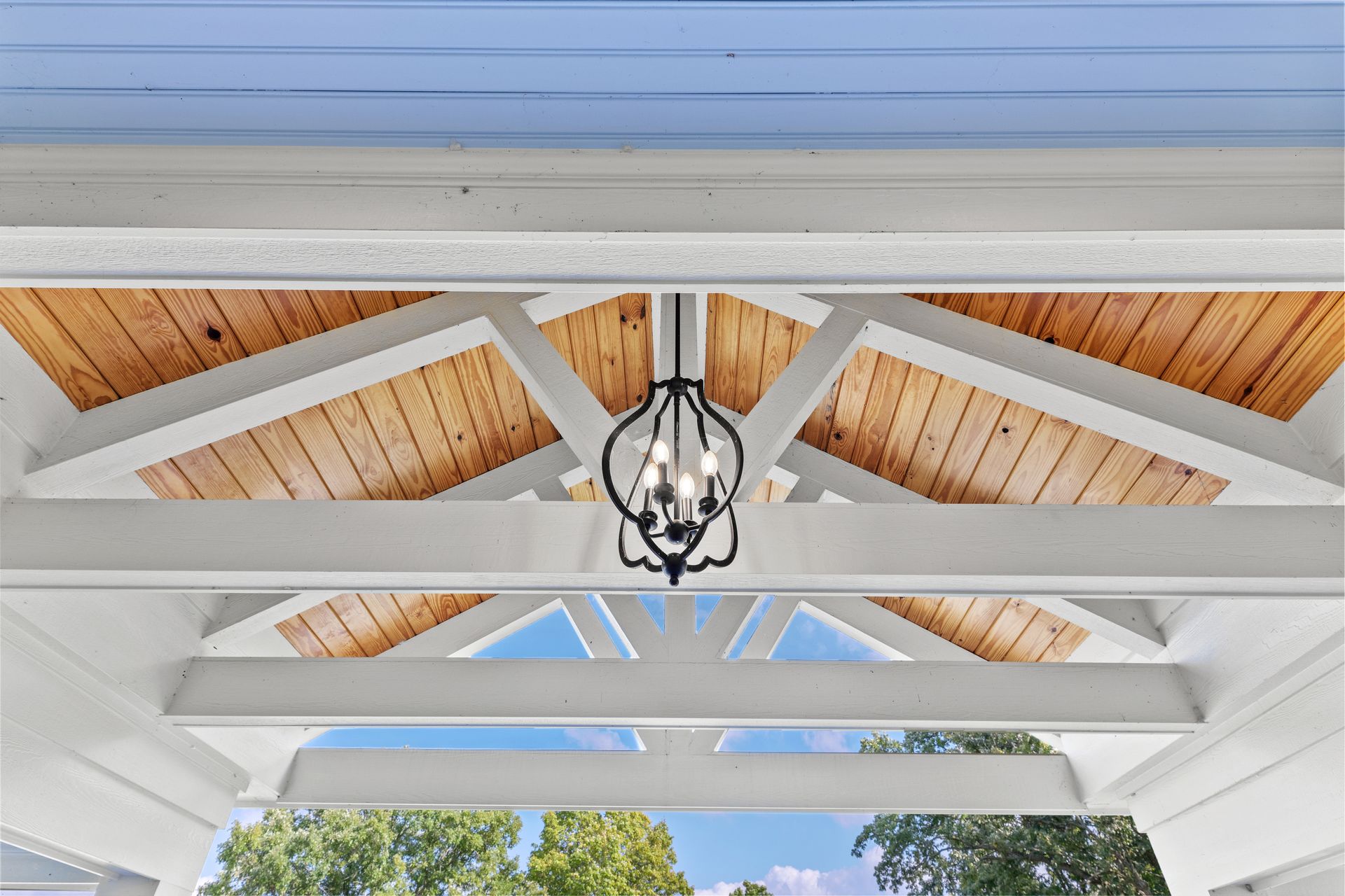 White porch with wood ceiling, black chandelier, and blue sky visible.