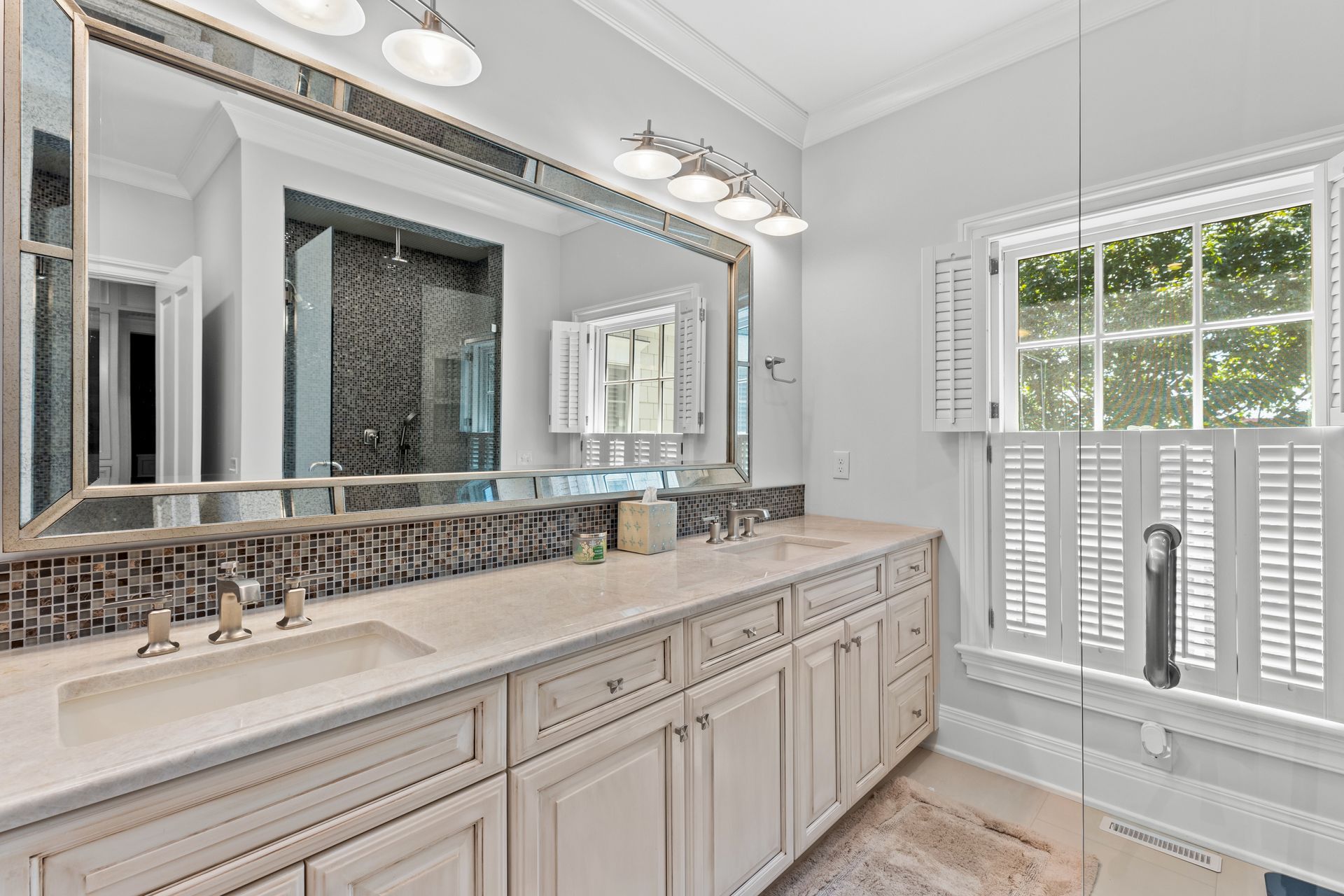 Bathroom with white vanity, large mirror, and window with shutters.