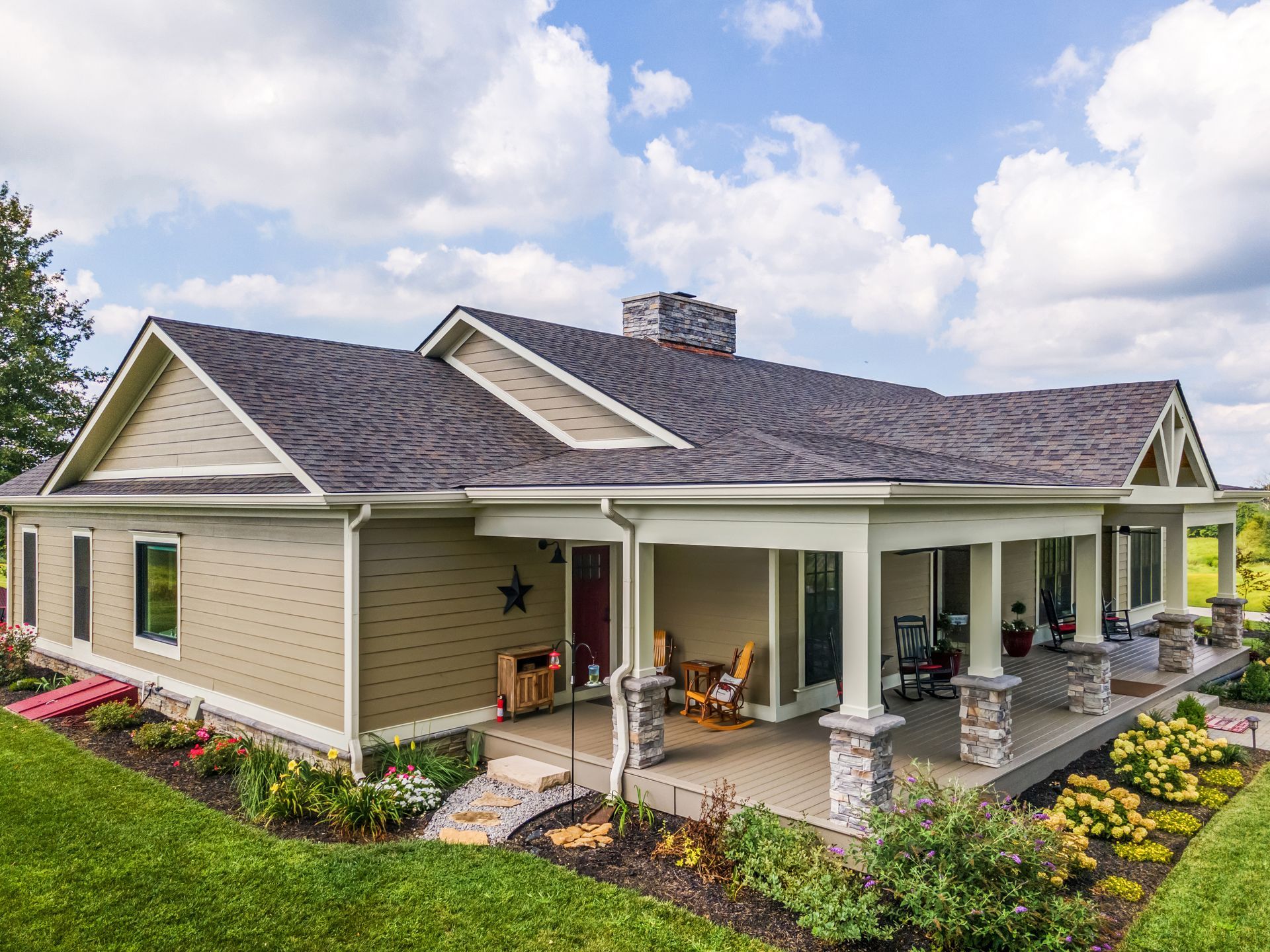 Beige ranch house with a large porch, green lawn, and blue sky.