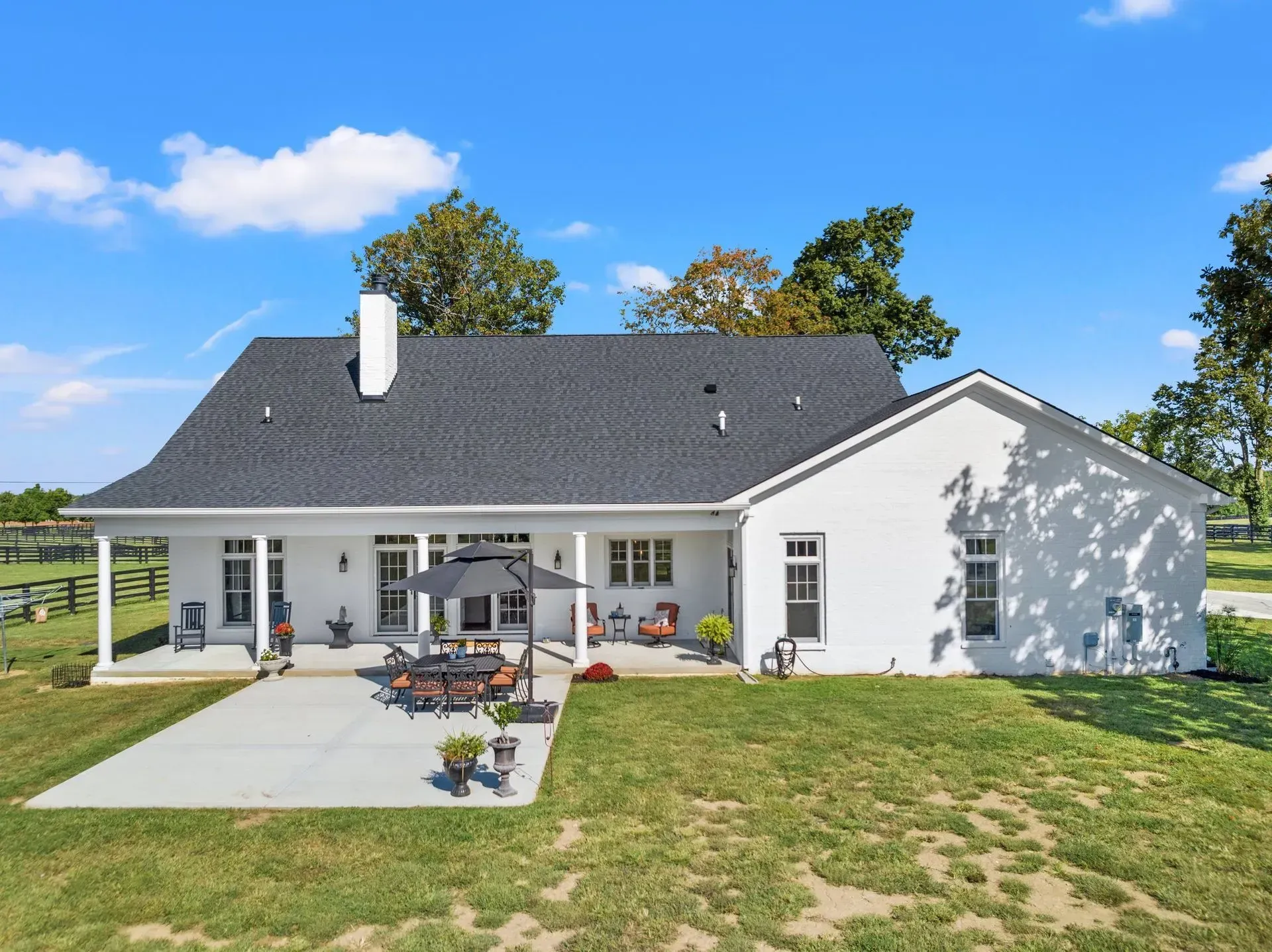White farmhouse with a black roof and patio furniture on a sunny day.