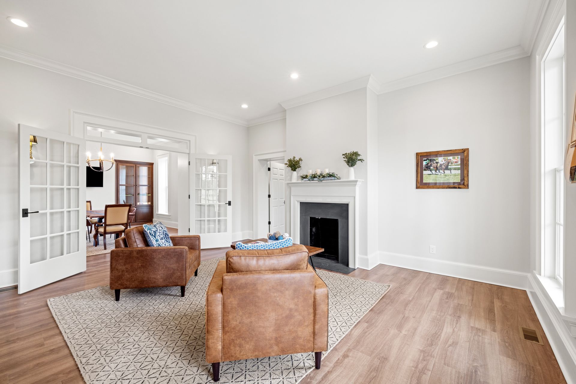 Living room with brown leather armchairs, fireplace, and French doors leading to dining area.