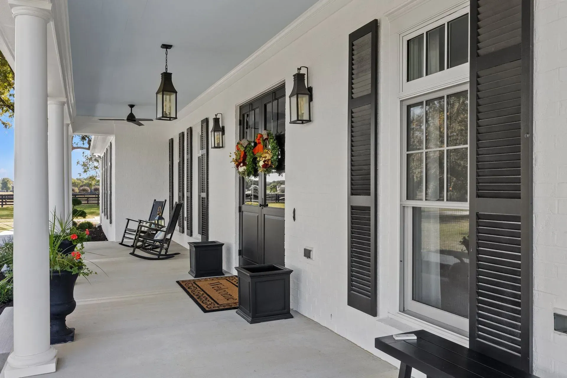 White porch with black shutters, lanterns, and rocking chairs. Door with wreath.