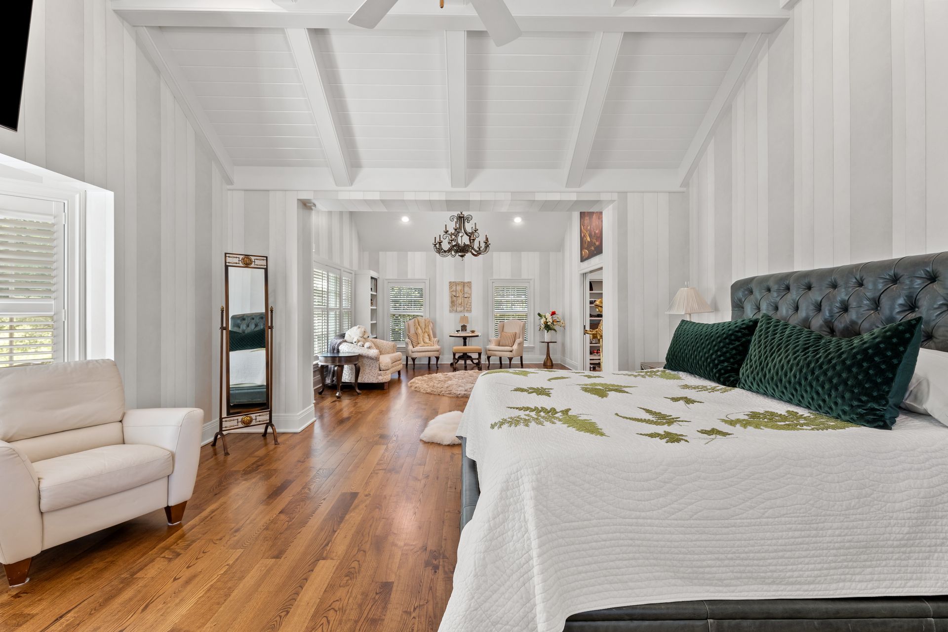 Spacious bedroom with hardwood floors, white panel walls, and a bed facing an open living area.