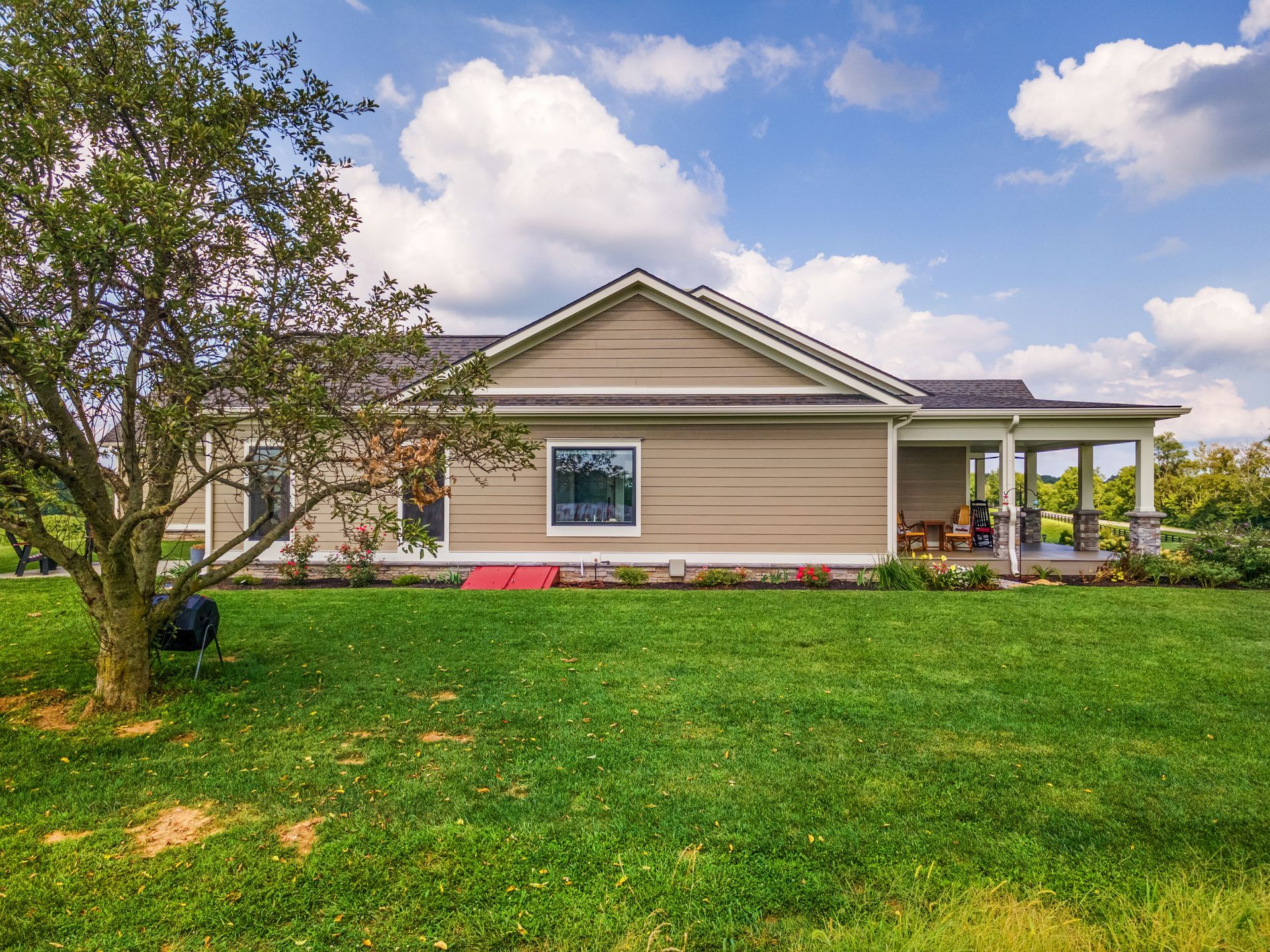Tan house with covered porch and green yard under a blue sky.