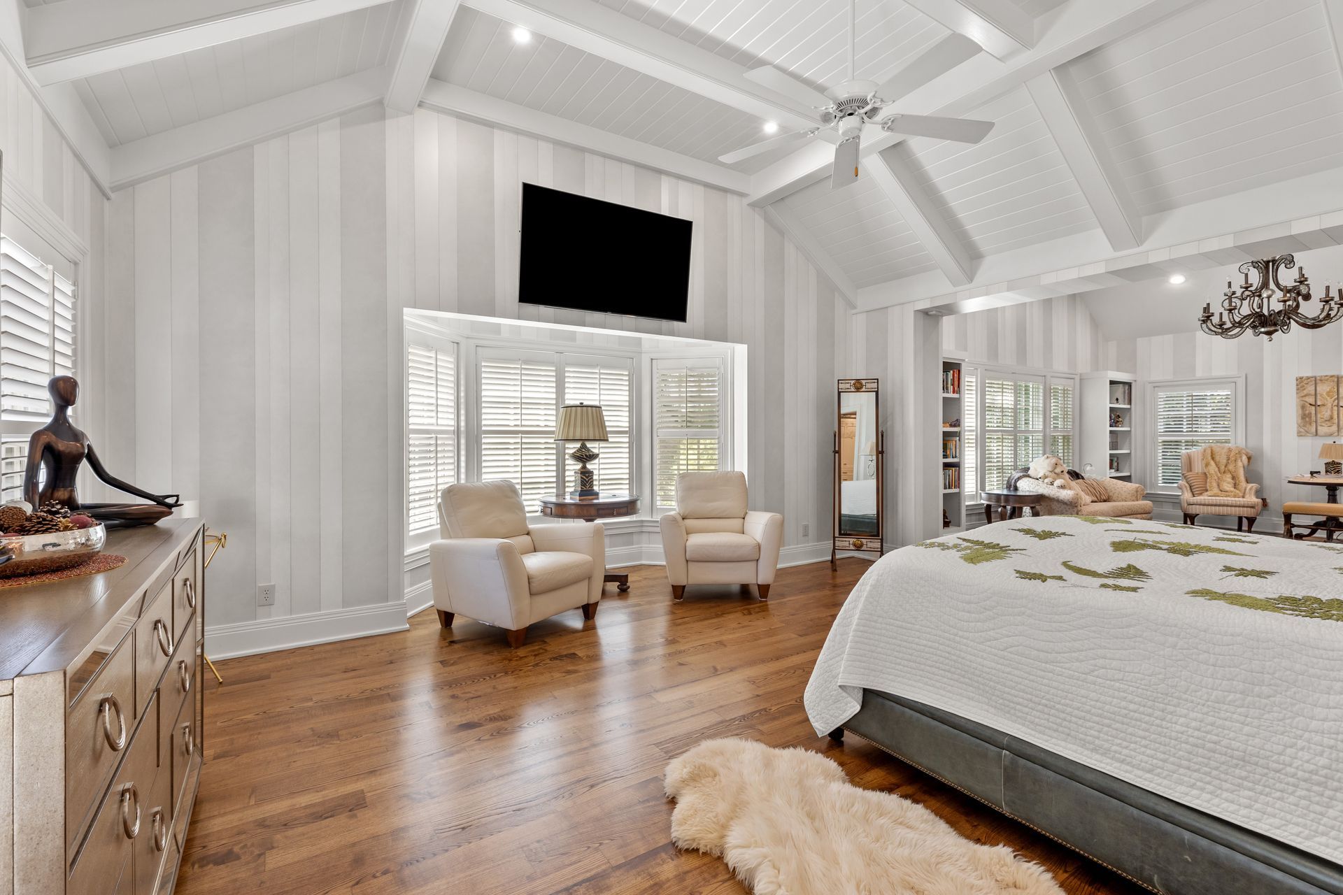Spacious bedroom with wood floors, striped walls, and vaulted ceiling; includes seating area, bed, and dresser.