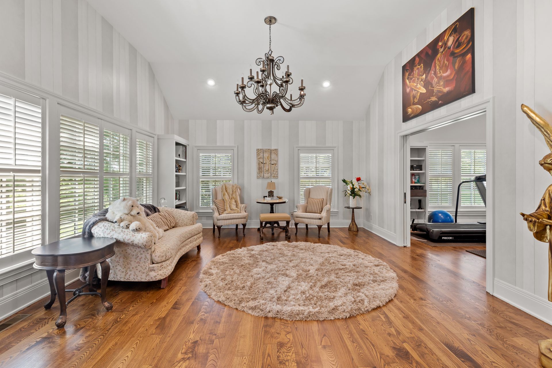 Living room with chandelier, round rug, and seating area; doorway to a home gym.