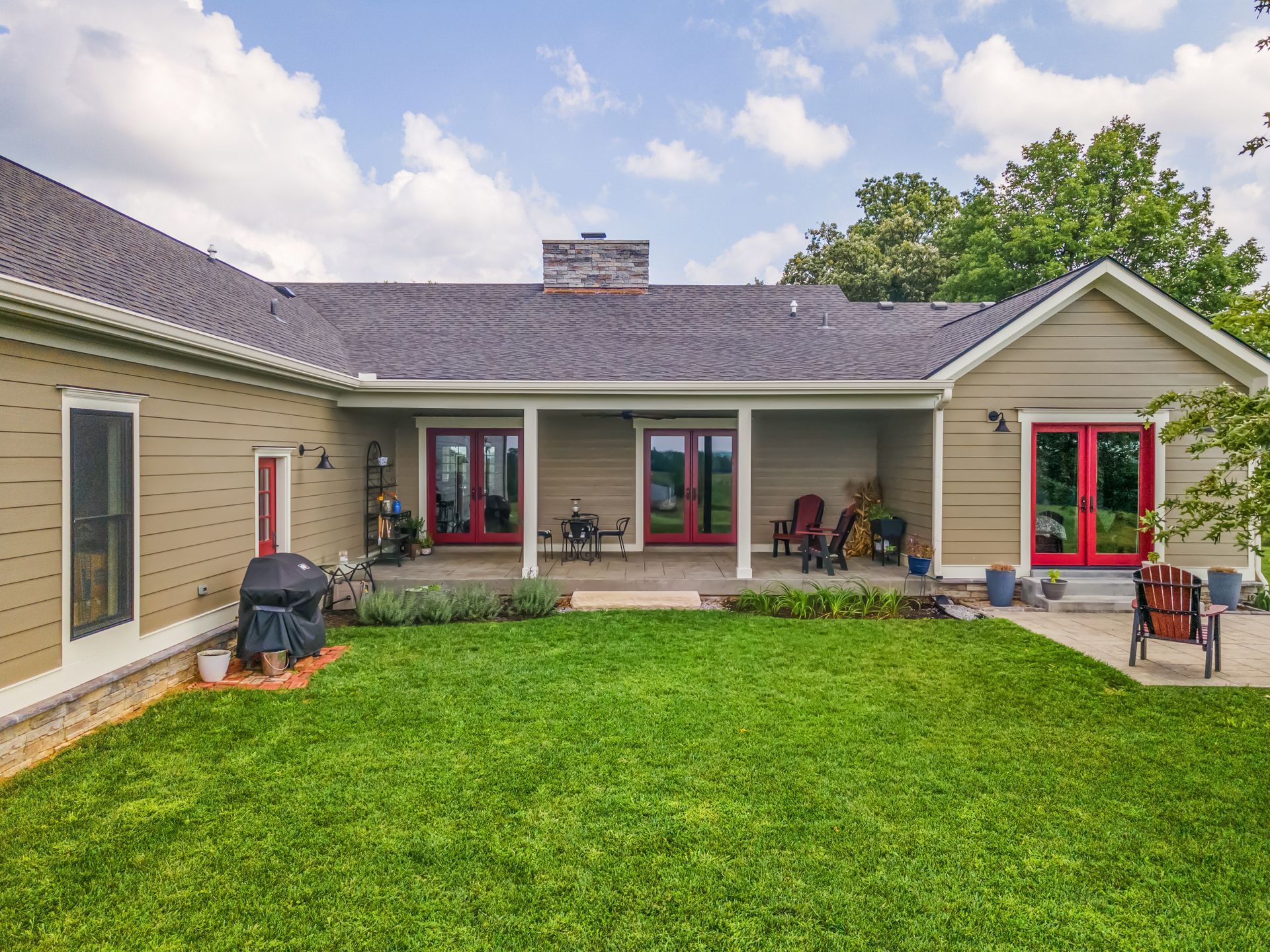 Backyard view of a house with red doors, green lawn, and a covered patio.