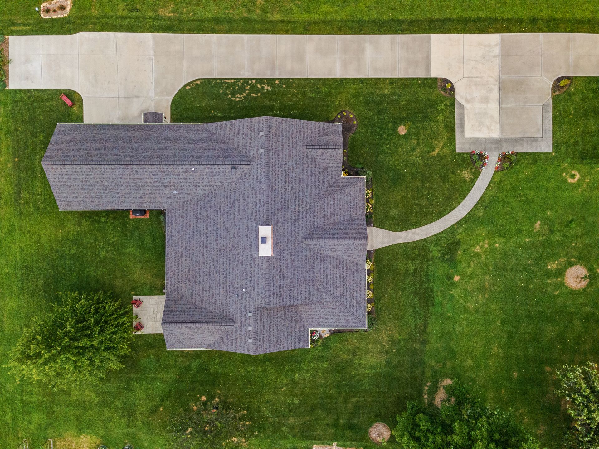 Overhead view of a house with a driveway and green yard. Gray roof, concrete driveway and a curving sidewalk.