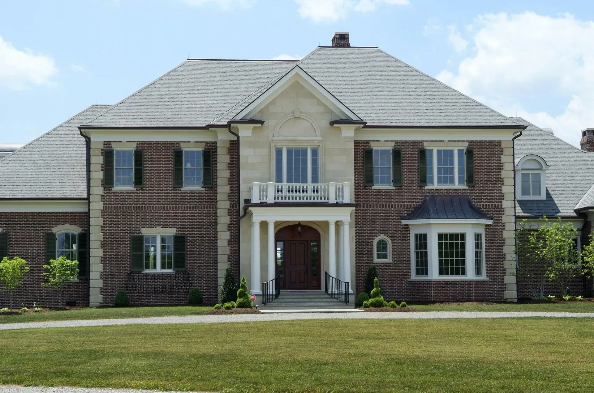 Large brick house with green shutters, white trim, and gray roof.
