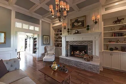 Cozy living room with fireplace, bookshelves, and chandelier. Hardwood floors, light blue walls, and comfortable furniture.